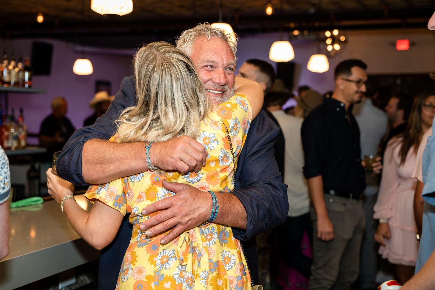 People sharing a warm embrace during a social gathering with ambient lighting.