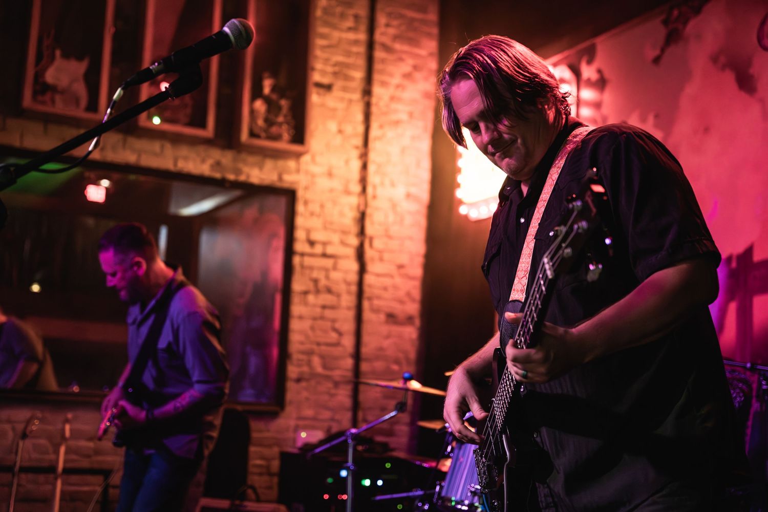 Band members performing on stage with red lighting against exposed brick walls.