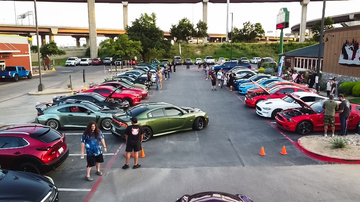 Car enthusiasts gather in a parking lot showcasing various sports and modified vehicles.
