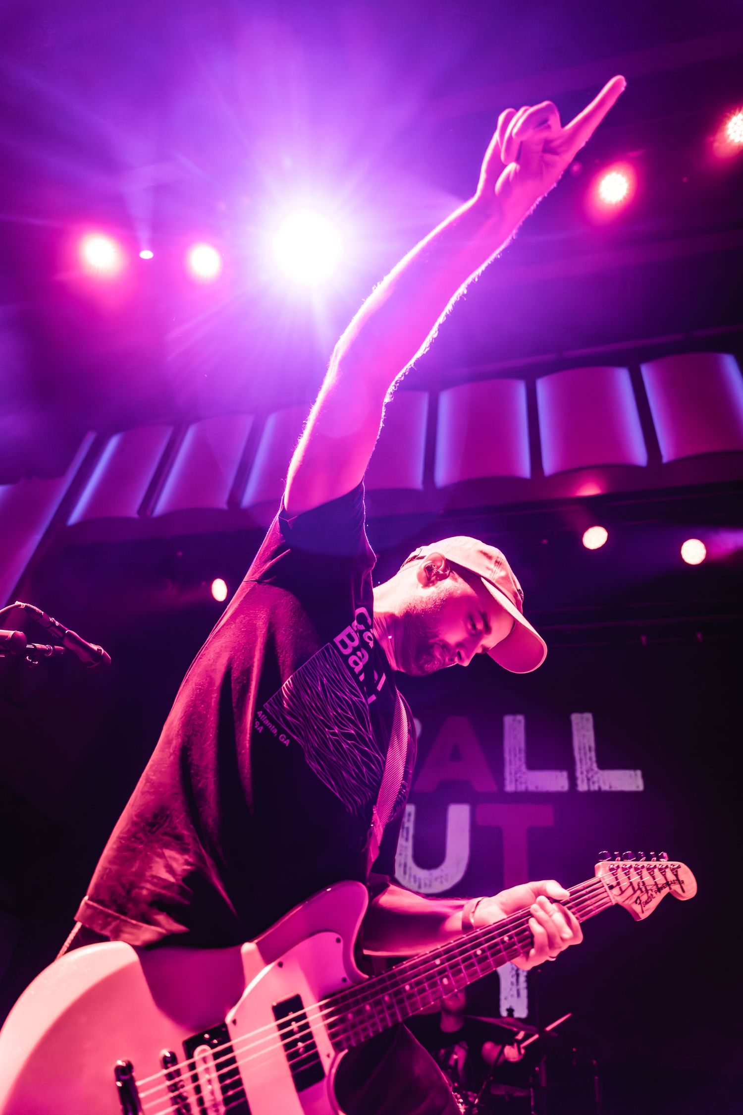Musician playing electric bass guitar performs on stage with dramatic purple lighting effects.