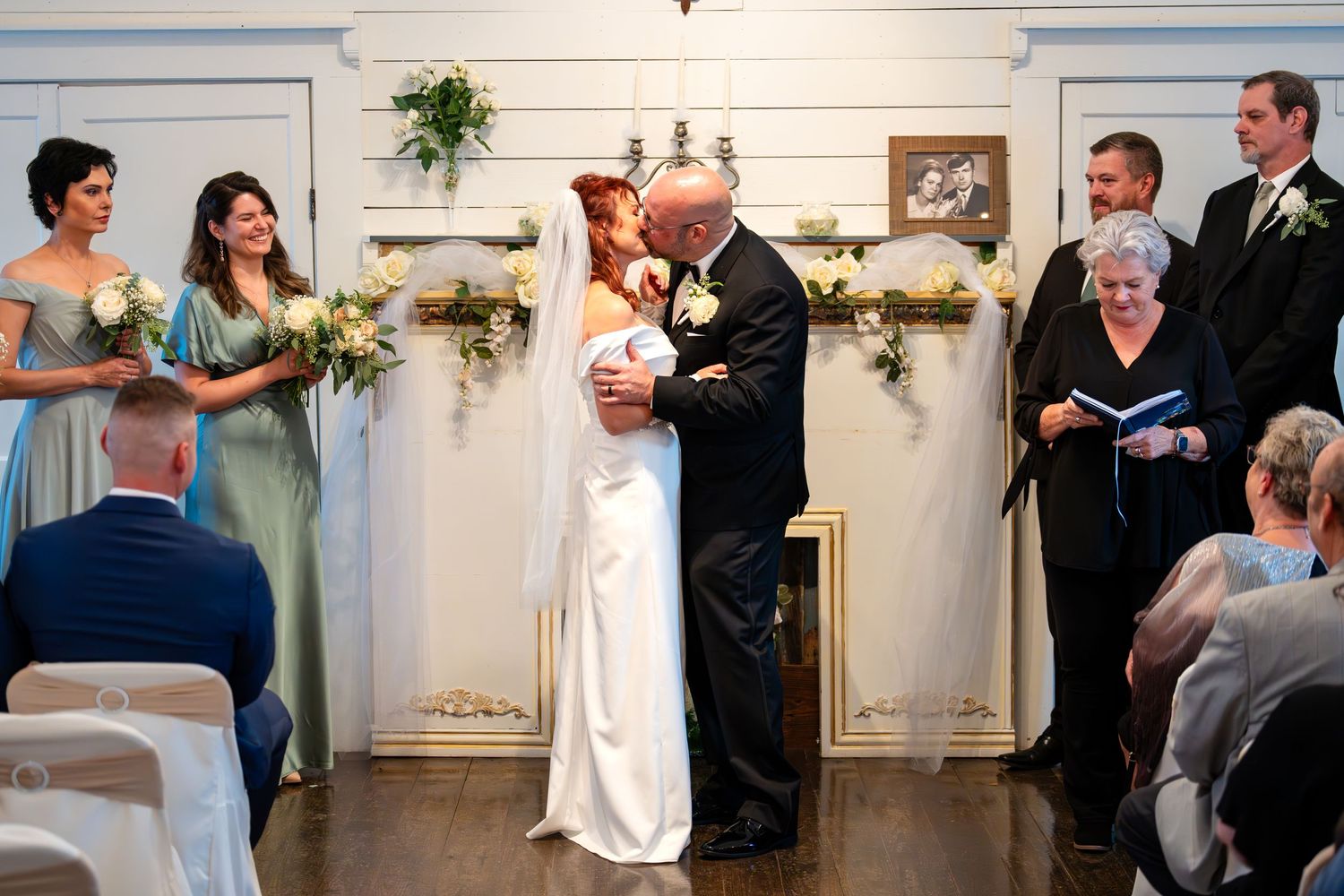 An indoor wedding ceremony with bridesmaids in gray dresses and guests watching the couple.