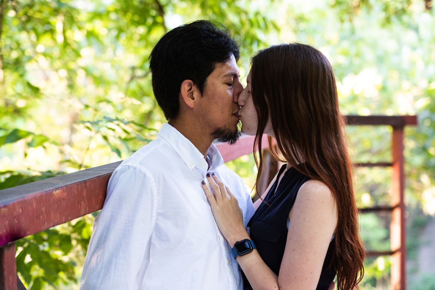 A romantic couple embraces tenderly against a natural background of trees and sunlight.