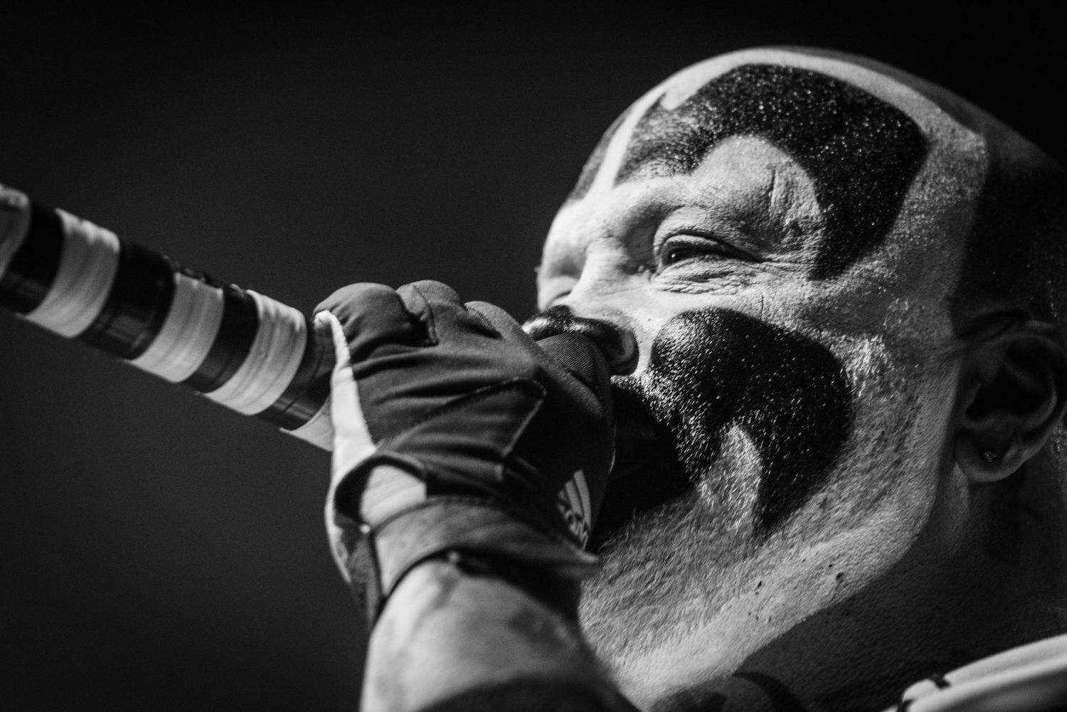 A dramatic black and white close-up of a performer with face paint singing intensely into a microphone.