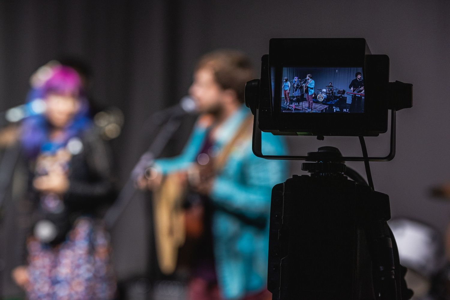 Video camera monitor shows live performance being filmed on dark stage.