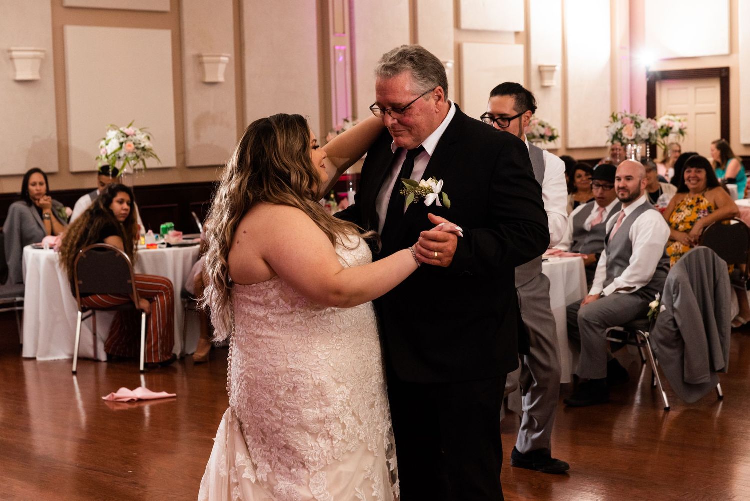 A couple shares an intimate dance moment at their wedding reception on a hardwood floor surrounded by guests.