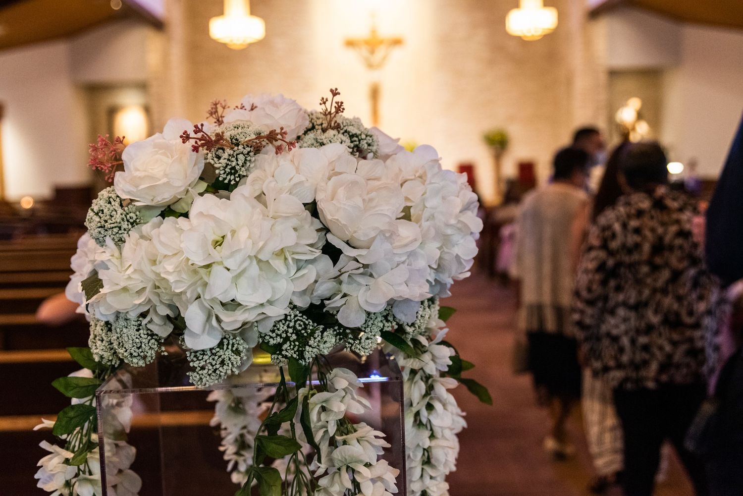 Elegant white and blush floral arrangement decorates church pews for wedding ceremony.