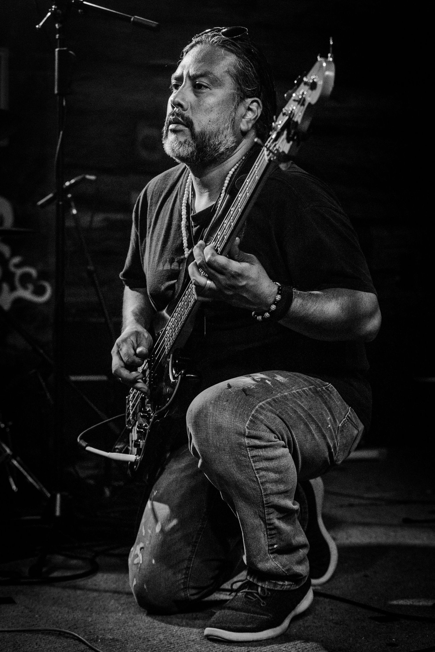 Bass player kneeling on stage performs passionately during dark concert setting.