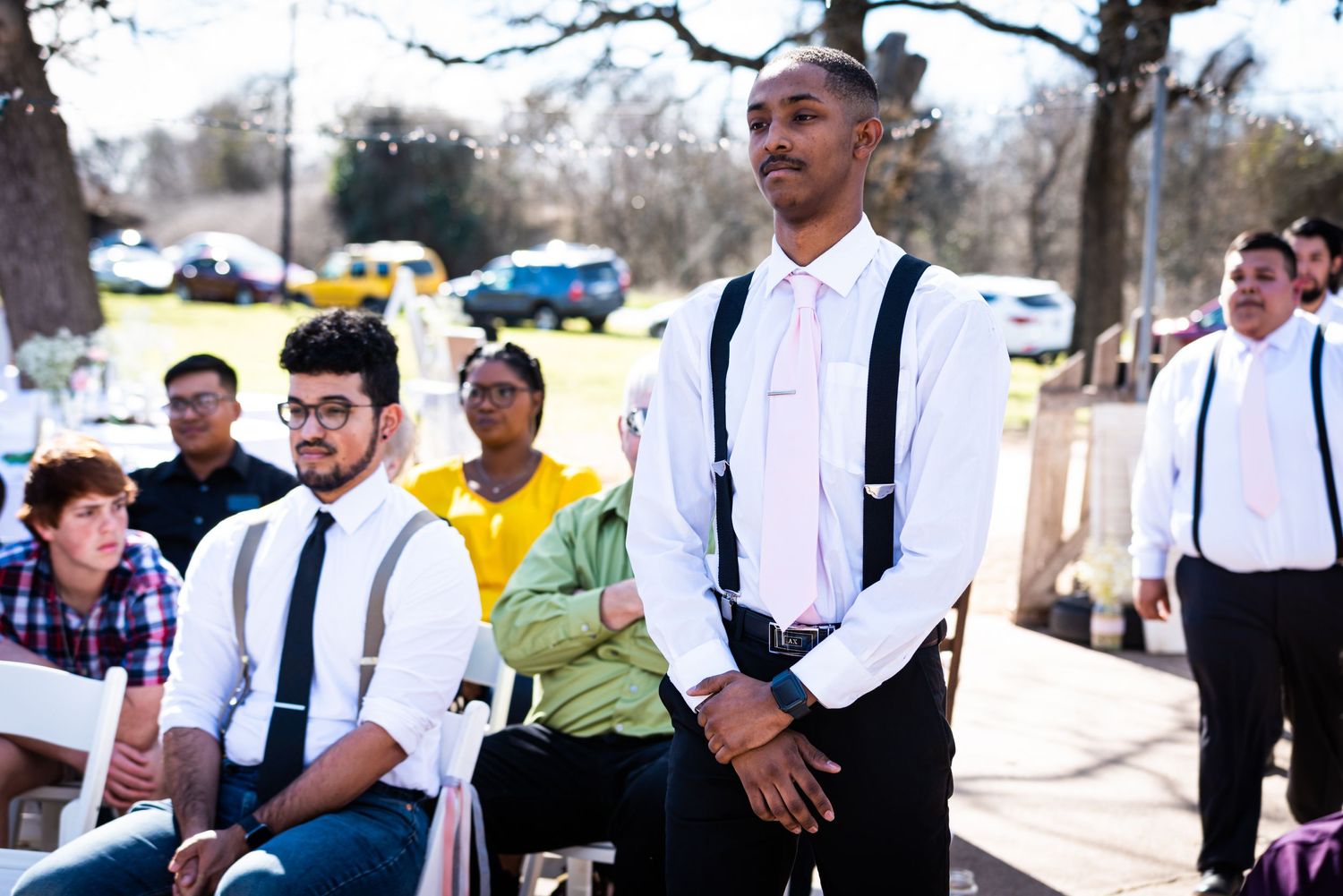 Wedding party members in white shirts and suspenders standing outdoors.