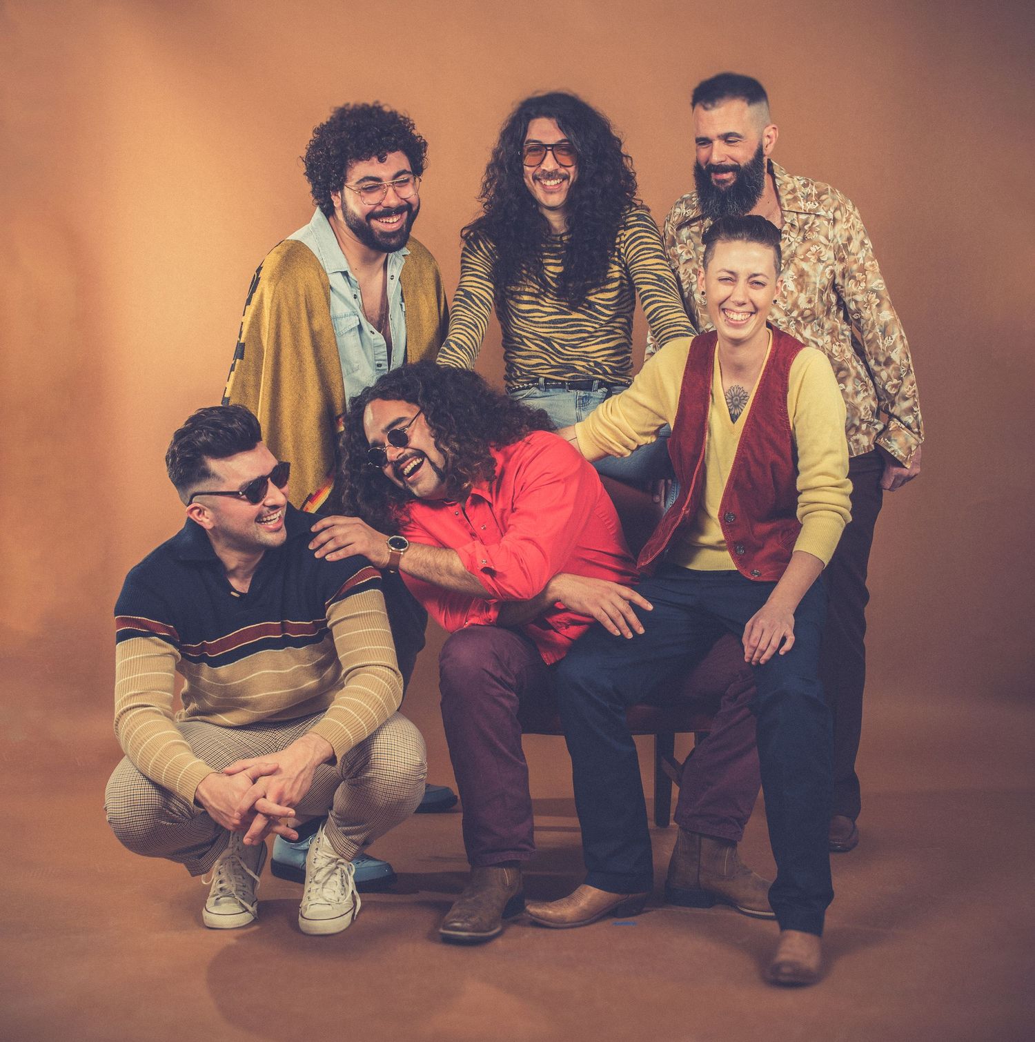 Band members in retro clothing arranged in casual group pose with warm lighting.