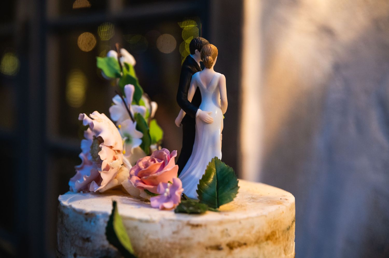Wedding cake topper figurines on display with soft bokeh lighting effects.