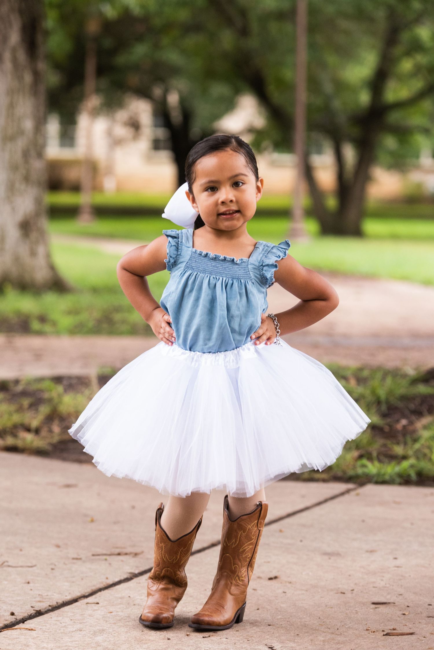 A dancer strikes a sassy pose in a white tutu, blue top and brown cowboy boots.