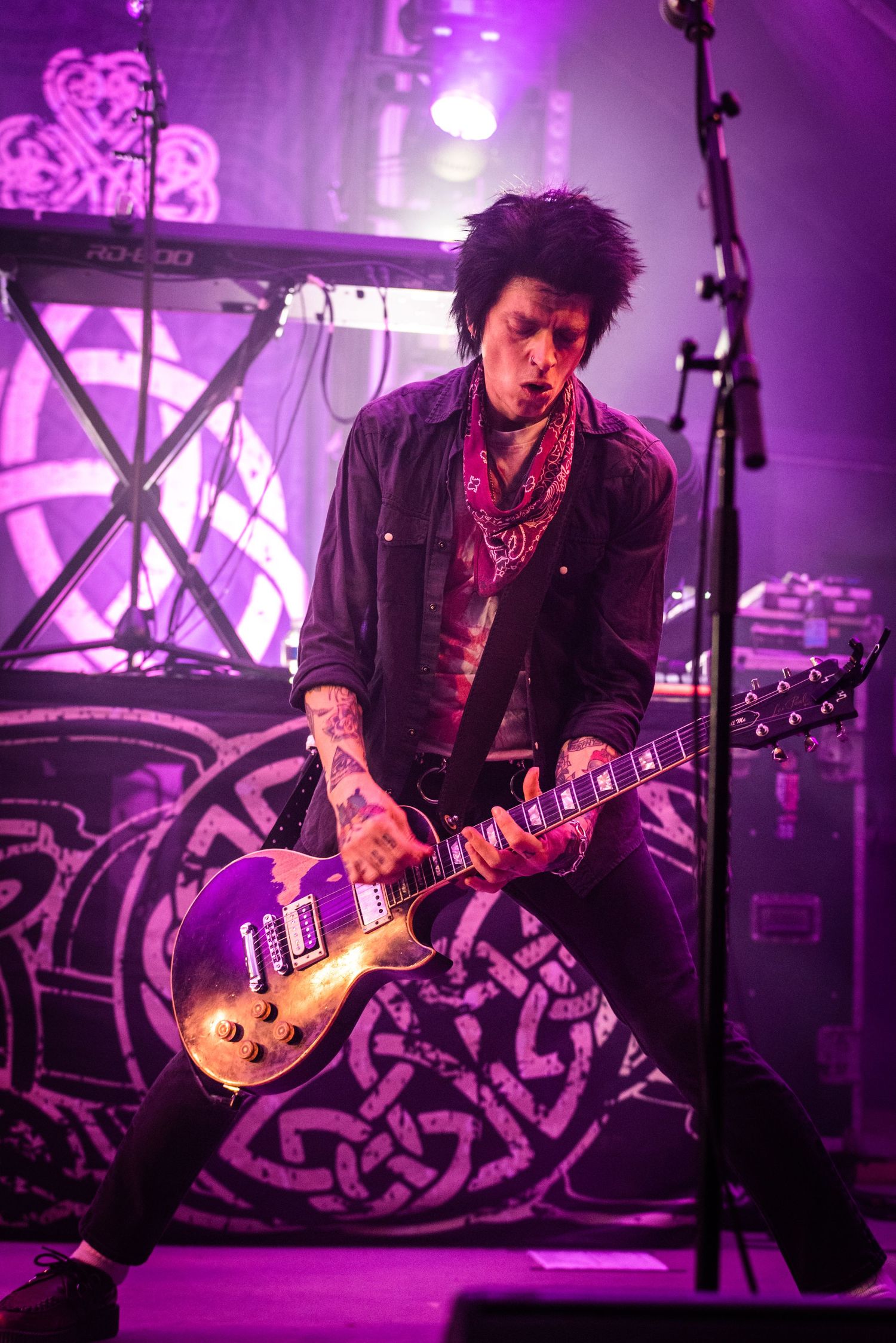 Guitar player performs with Les Paul guitar against purple stage lighting and decorative backdrop.
