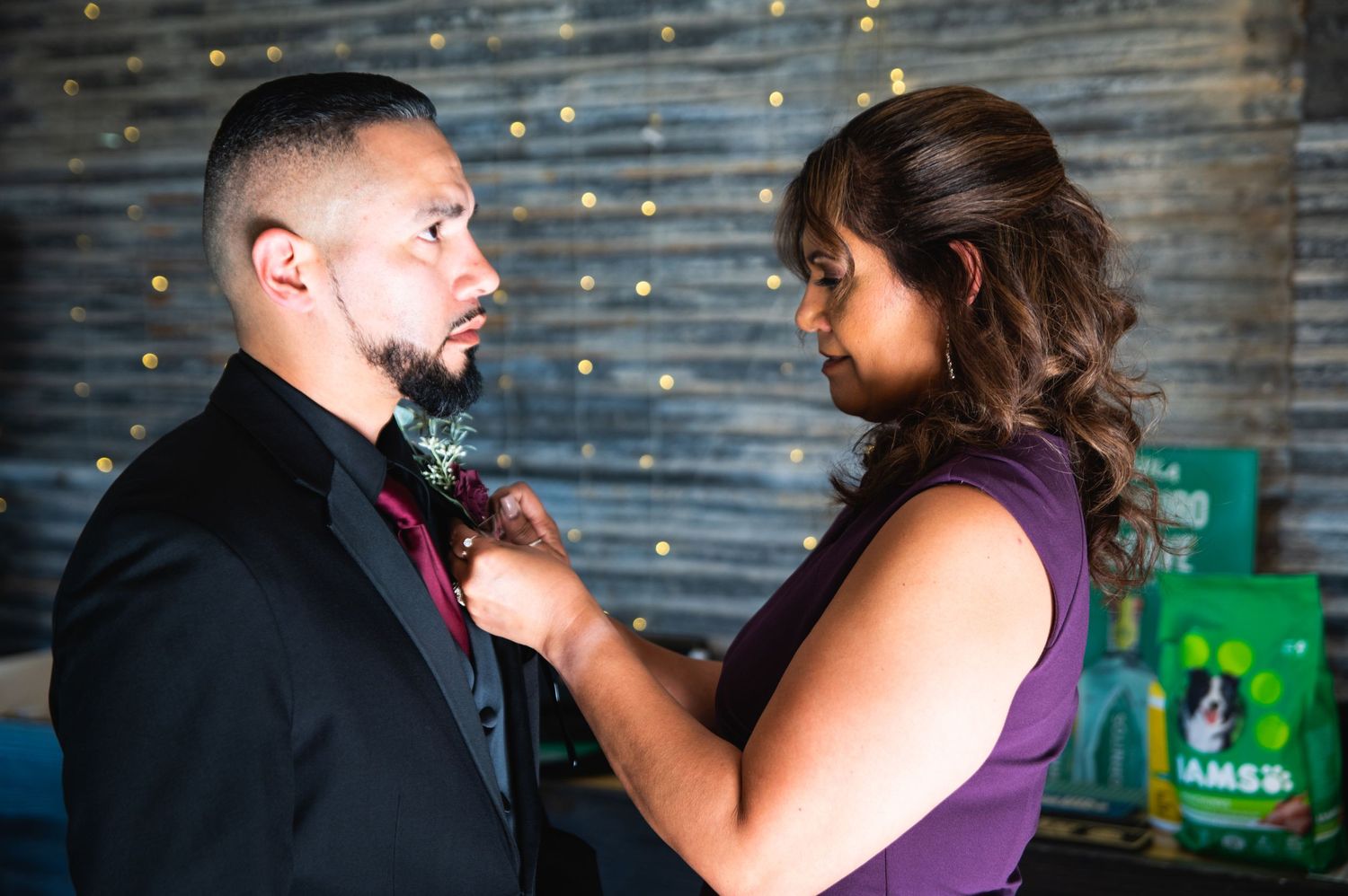 A boutonniere is being pinned on formal attire in an indoor setting with decorative lights.