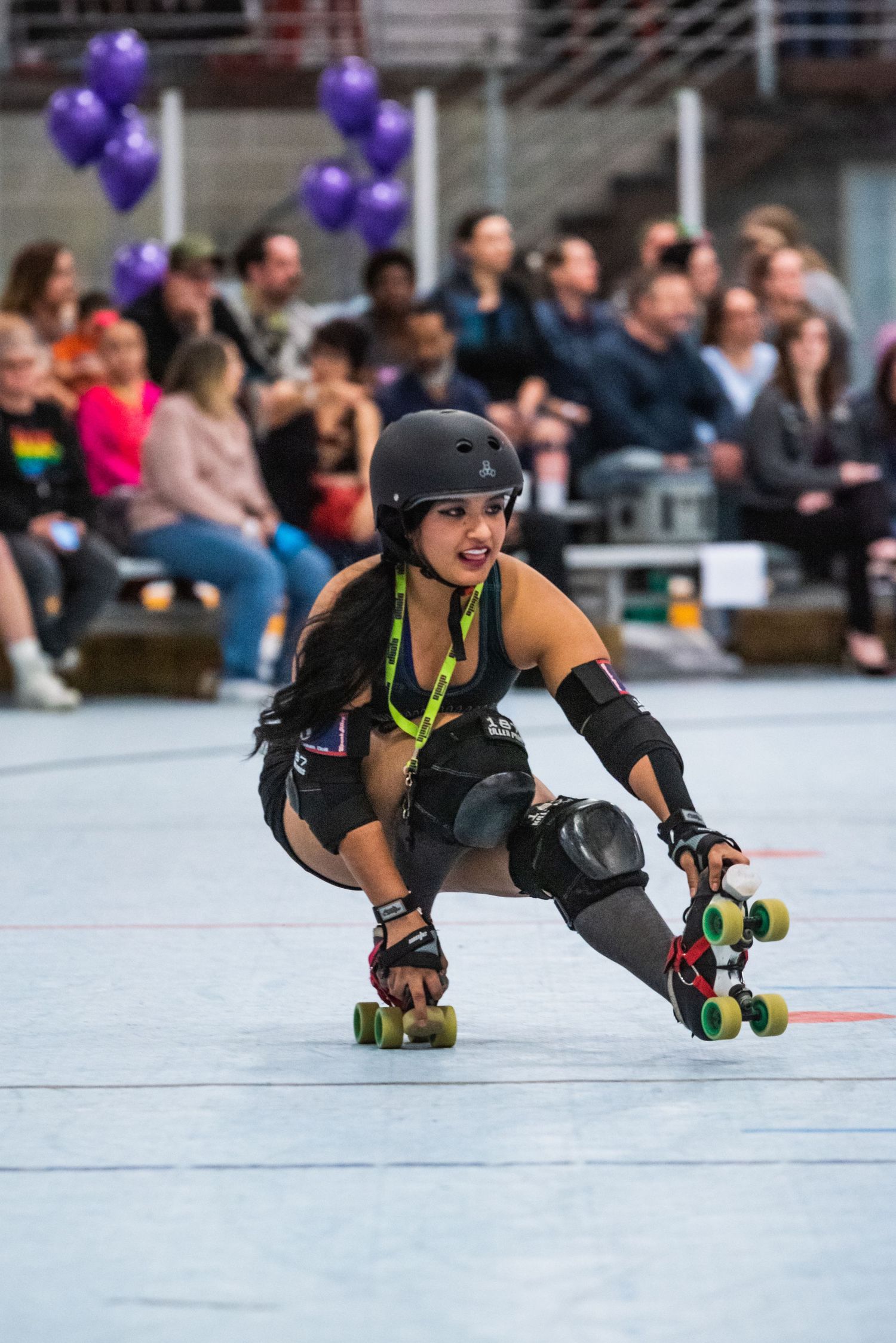 Roller derby skater performs low crouch maneuver on indoor rink.