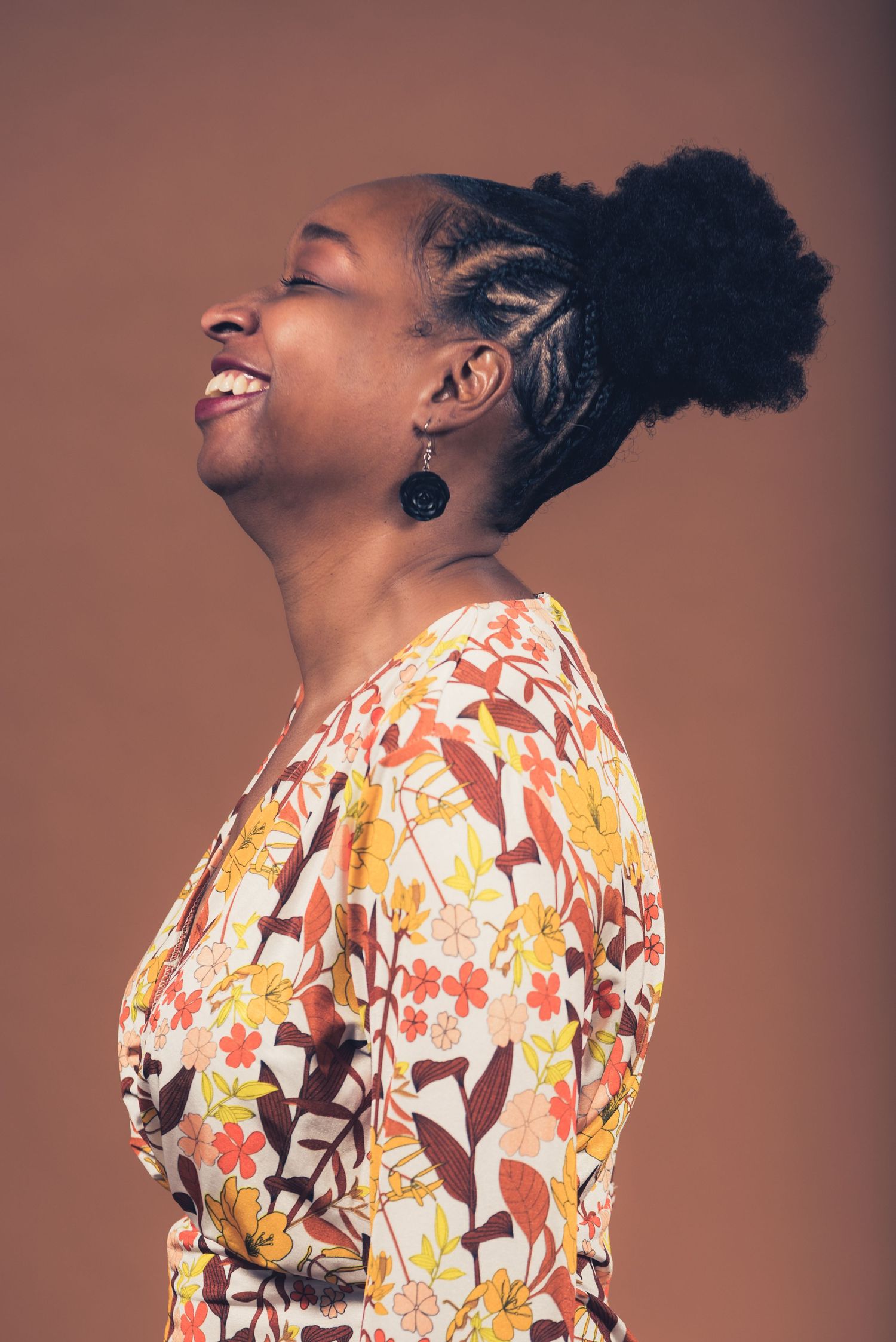 Profile shot of person in floral dress with braided hairstyle laughing joyfully.