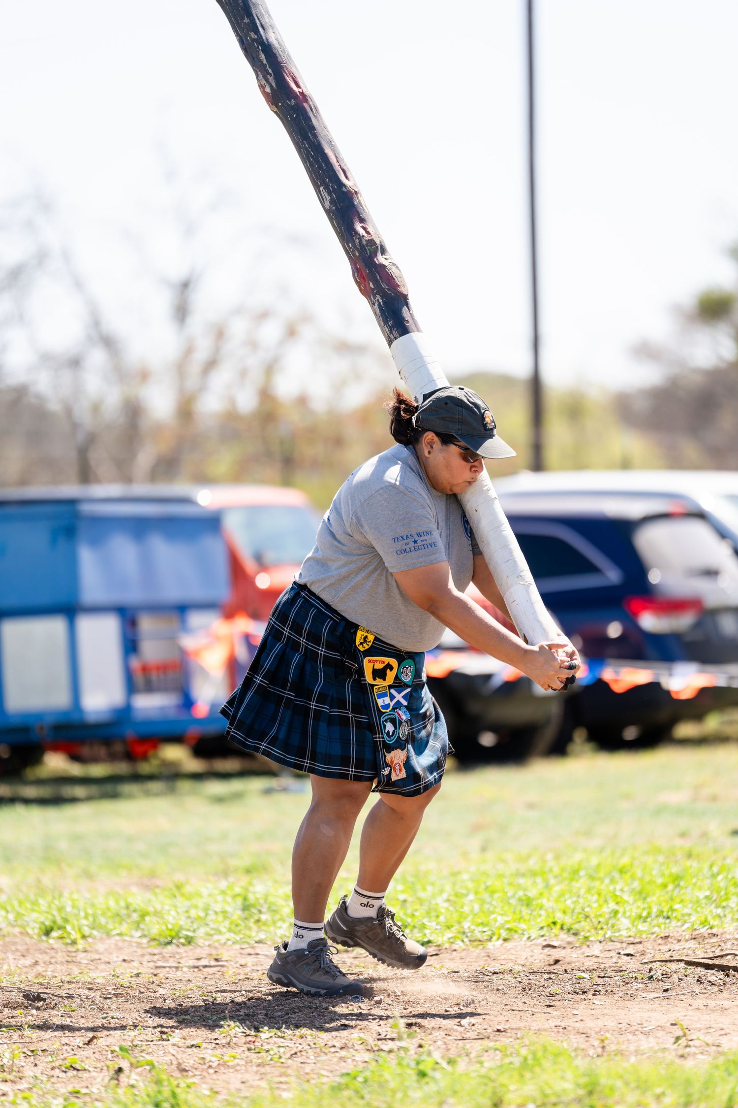 Person in a kilt competing in a caber toss at a Scottish Highland Games event outdoors.