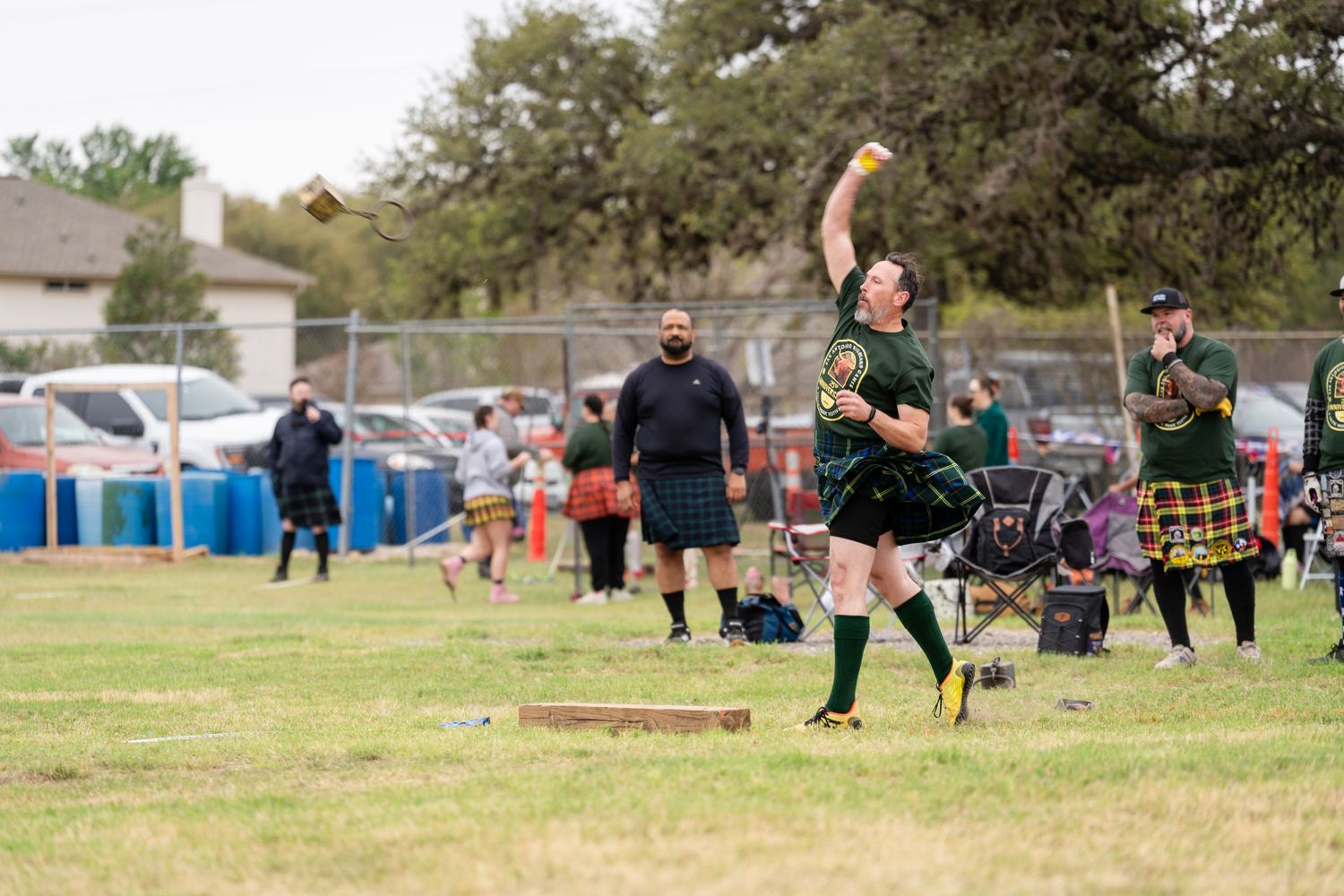 Athlete in green kilt throws object at Highland Games competition outdoors.