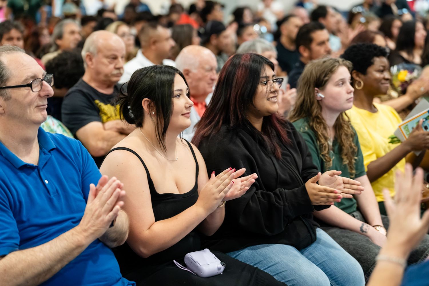 Diverse crowd of people clapping and smiling at an indoor event or ceremony.
