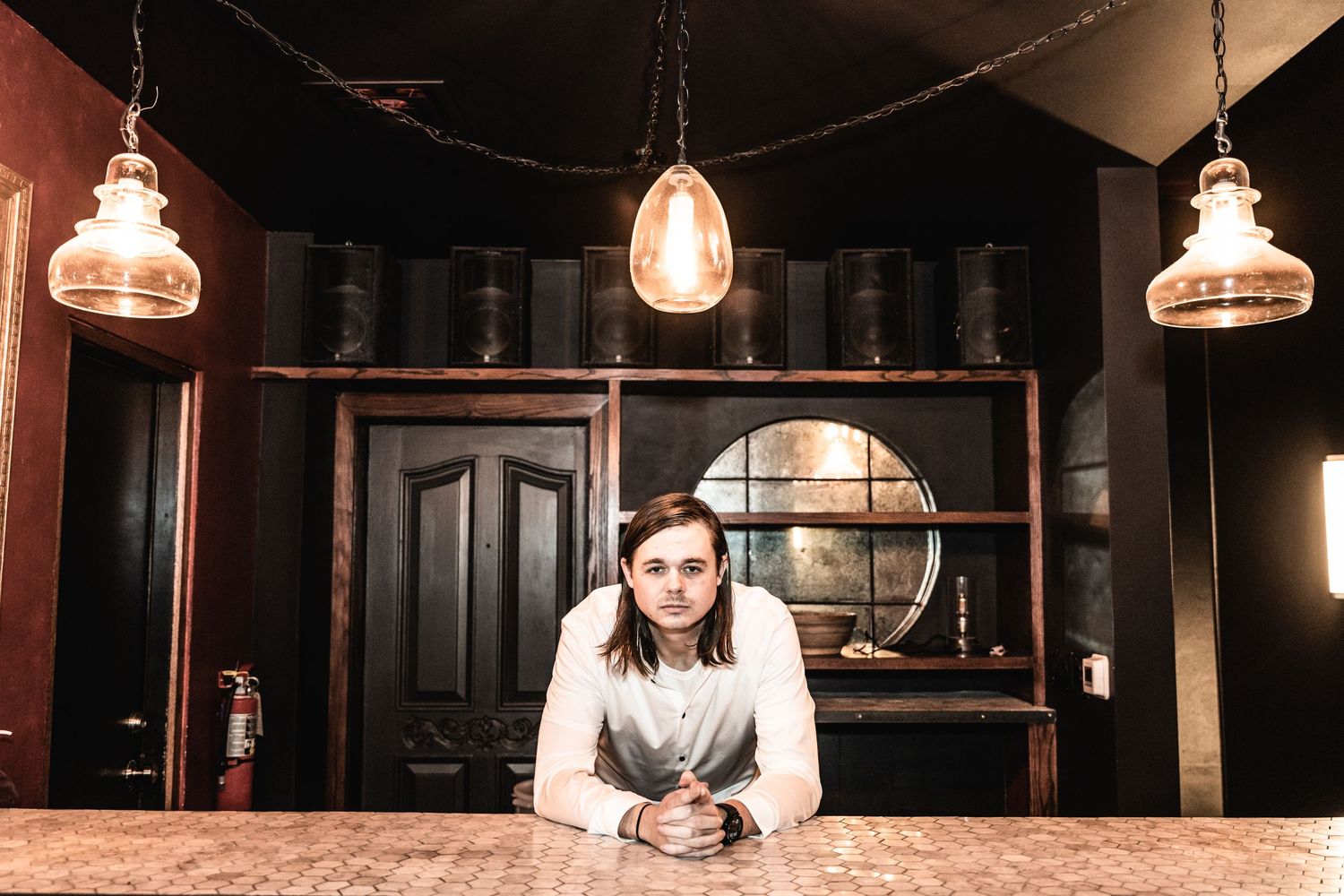 A panoramic view of a dimly lit bar interior with pendant lights hanging over a long wooden counter.