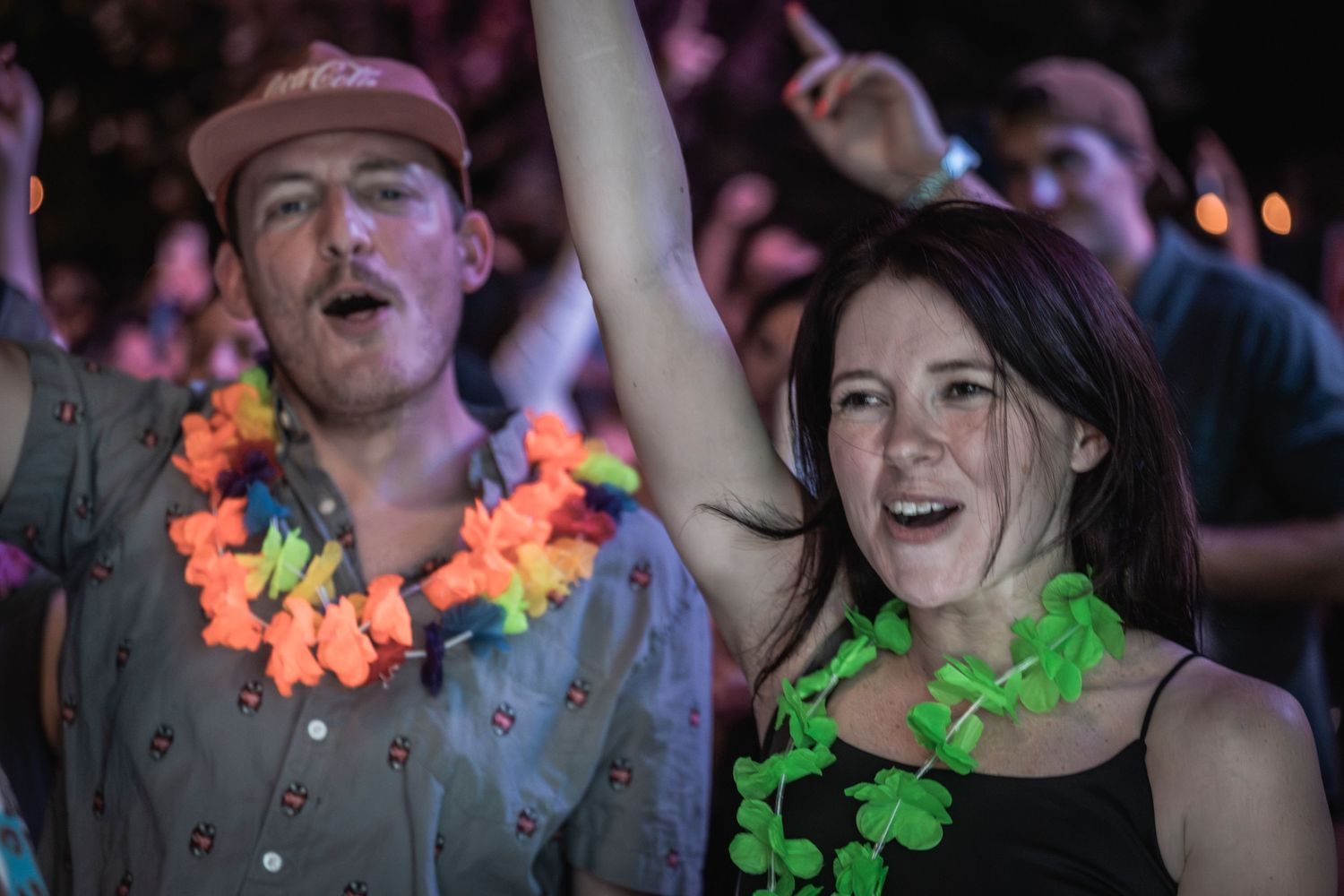 People dancing and celebrating at a party wearing colorful floral leis and festive attire.