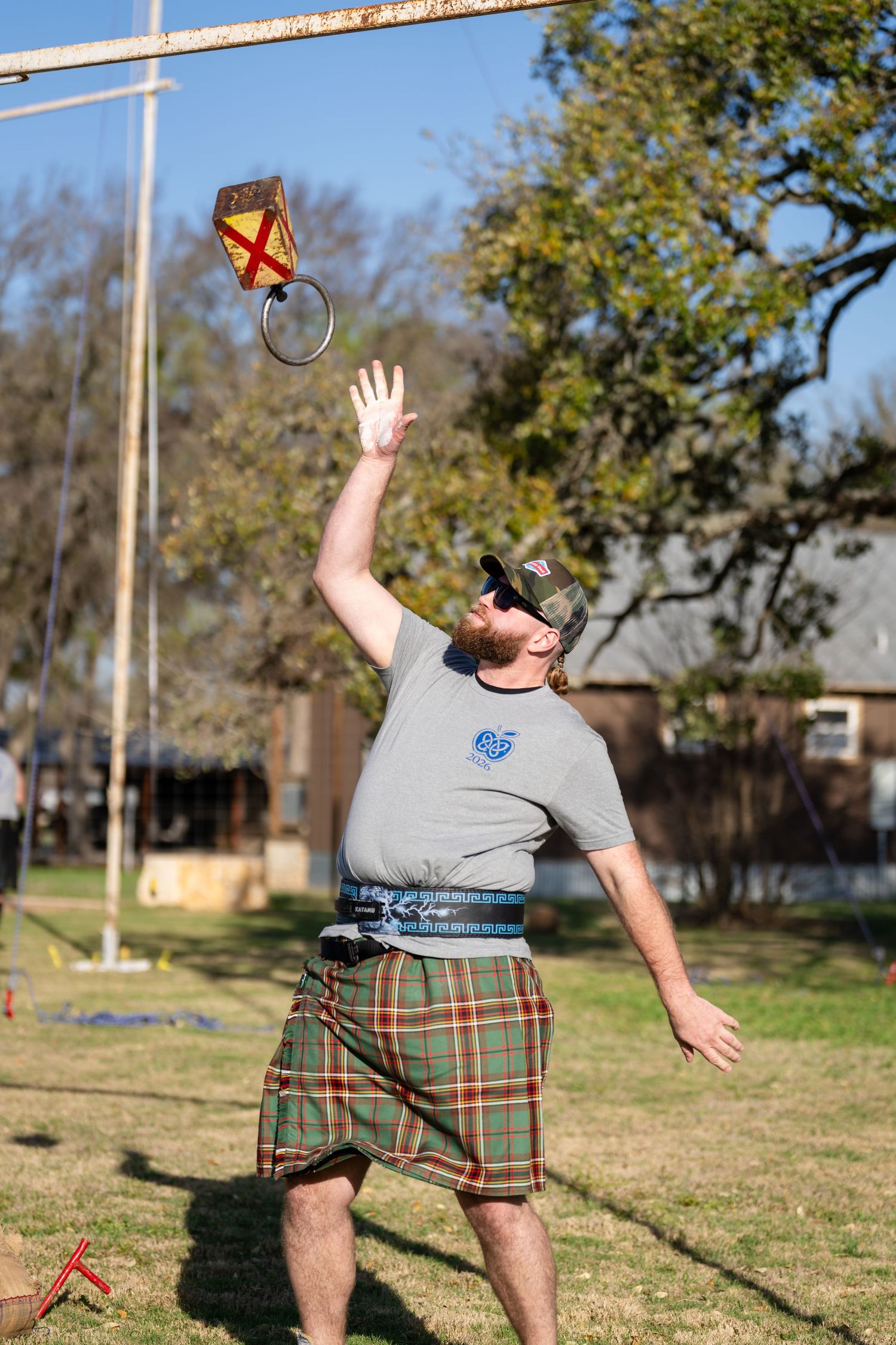 Man in tartan kilt tossing a ring onto a pole during a Scottish Highland Games competition outdoors.