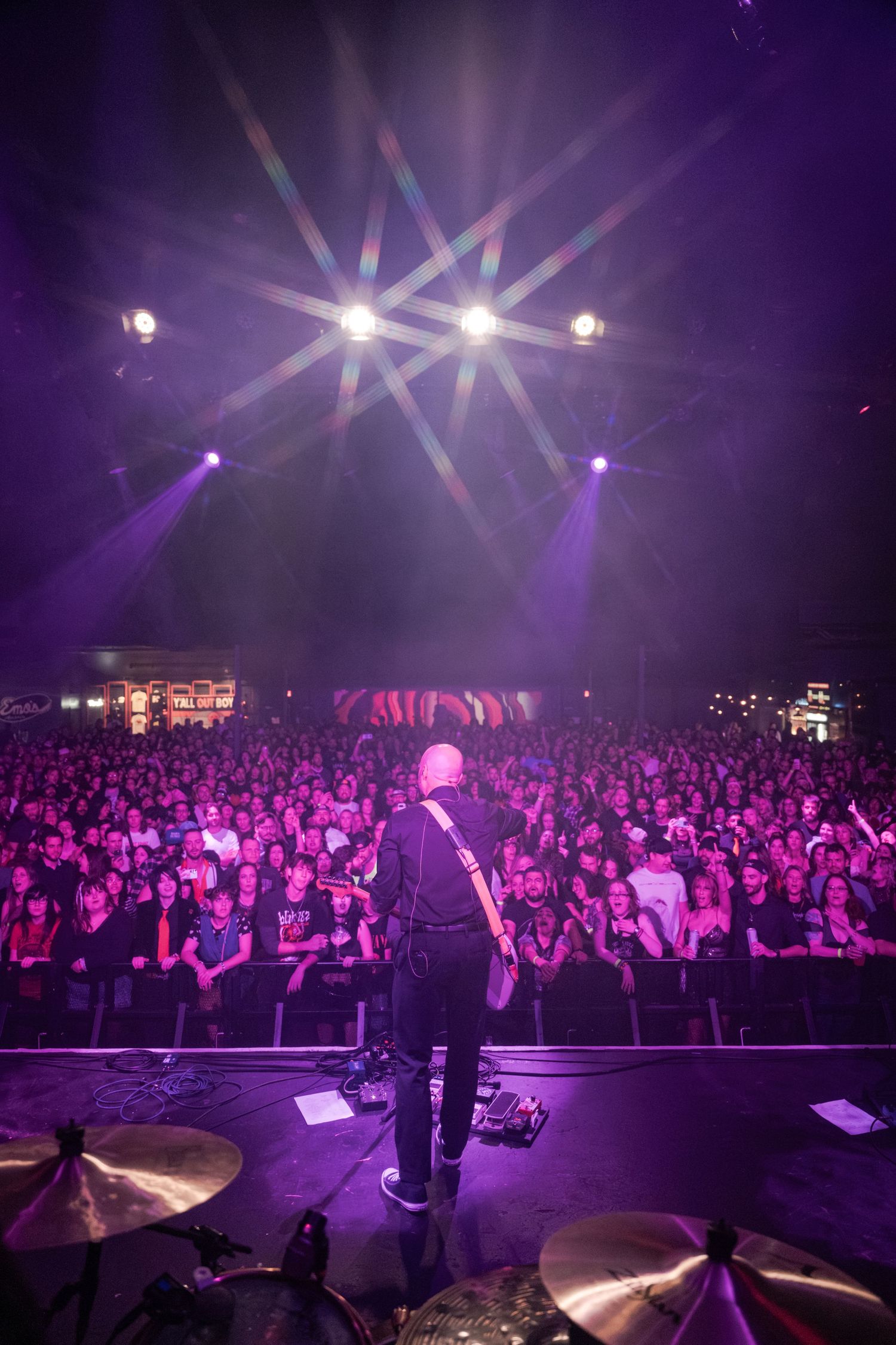 Guitarist performs on stage before a massive crowd under dramatic purple and white concert lights.