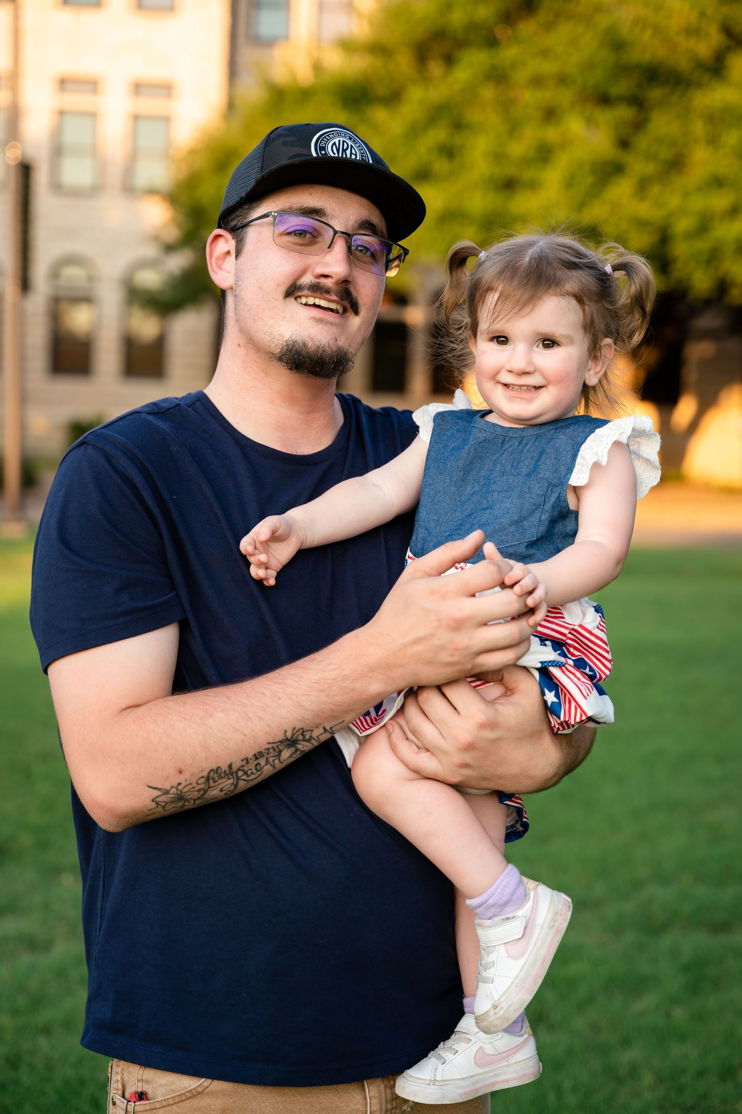 A tender family moment captured on a grassy lawn with buildings in the background.