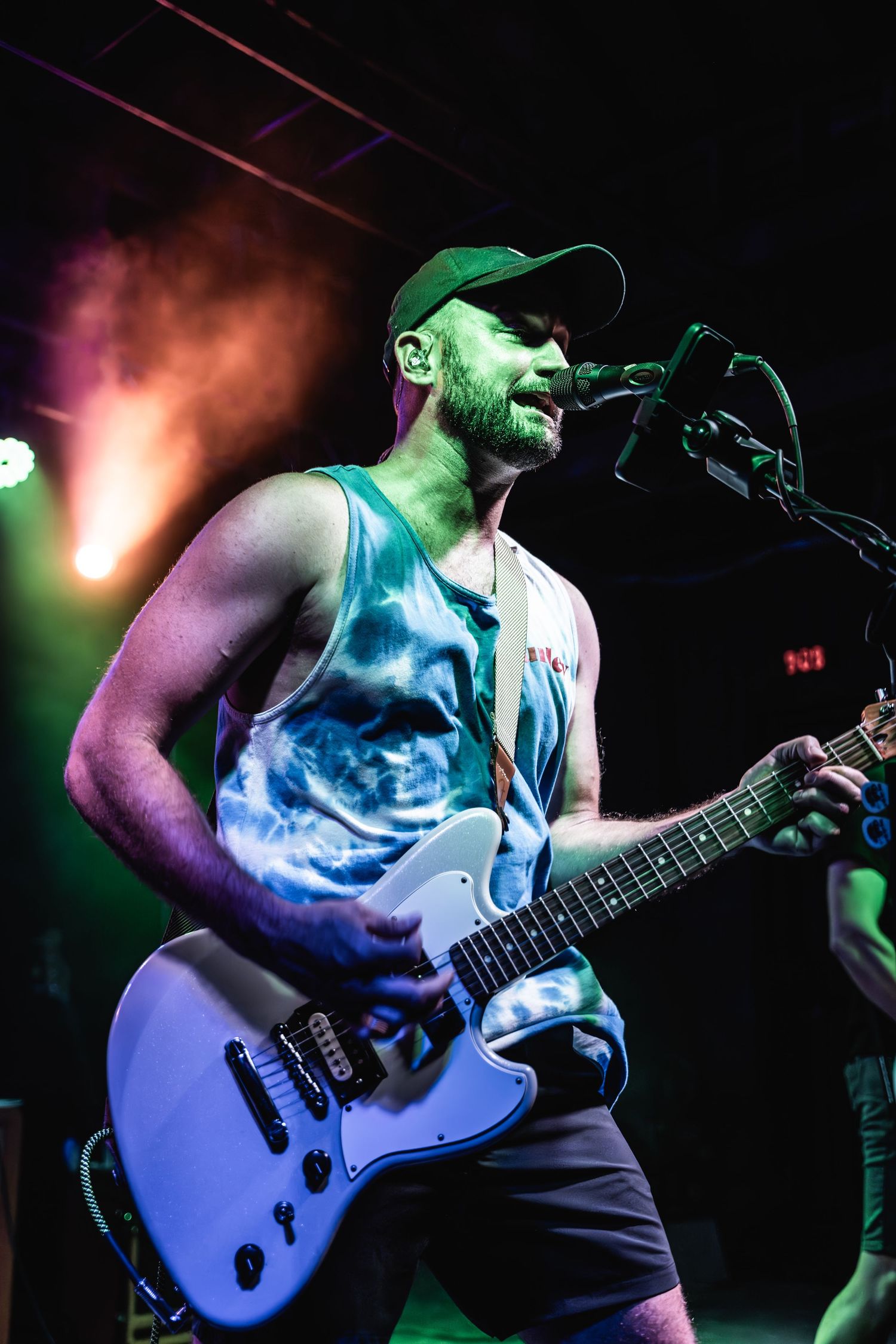Guitar player performs energetically on stage with colorful stage lighting and smoke effects.