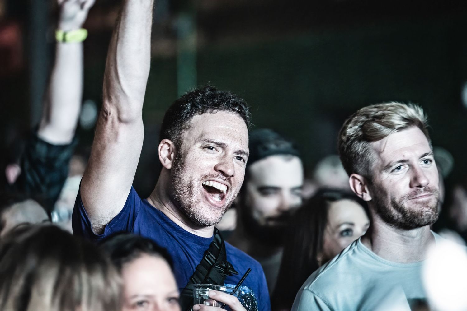 Enthusiastic concert-goers in crowd enjoying live music performance with raised arms.