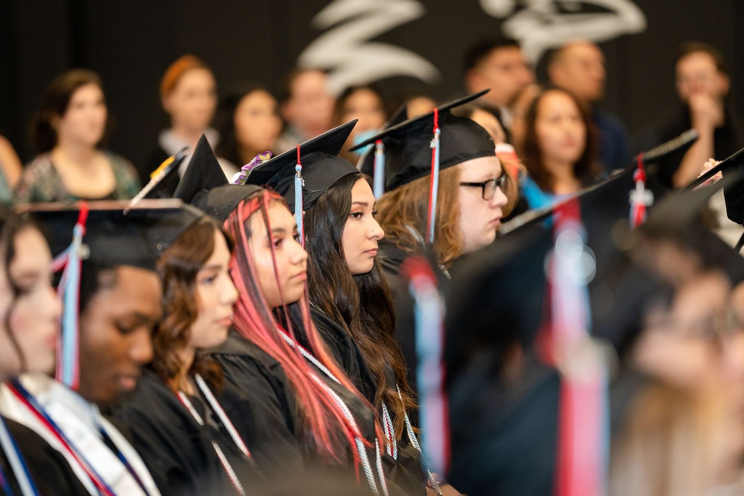 Graduates in black caps and gowns sit together during a commencement ceremony.