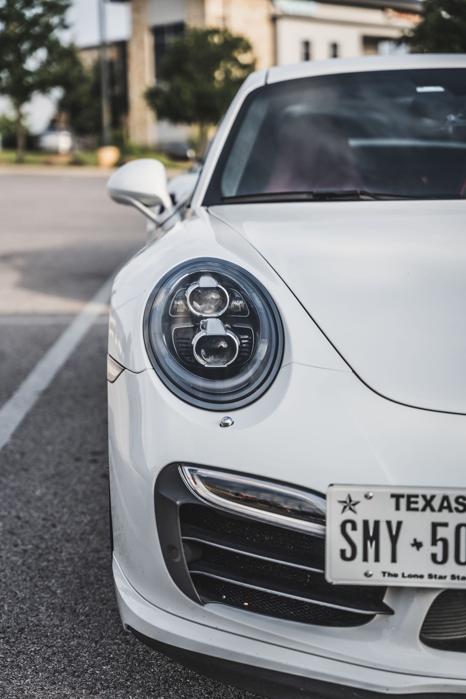 Front view of white Porsche 911 with round LED headlight and Texas license plate.