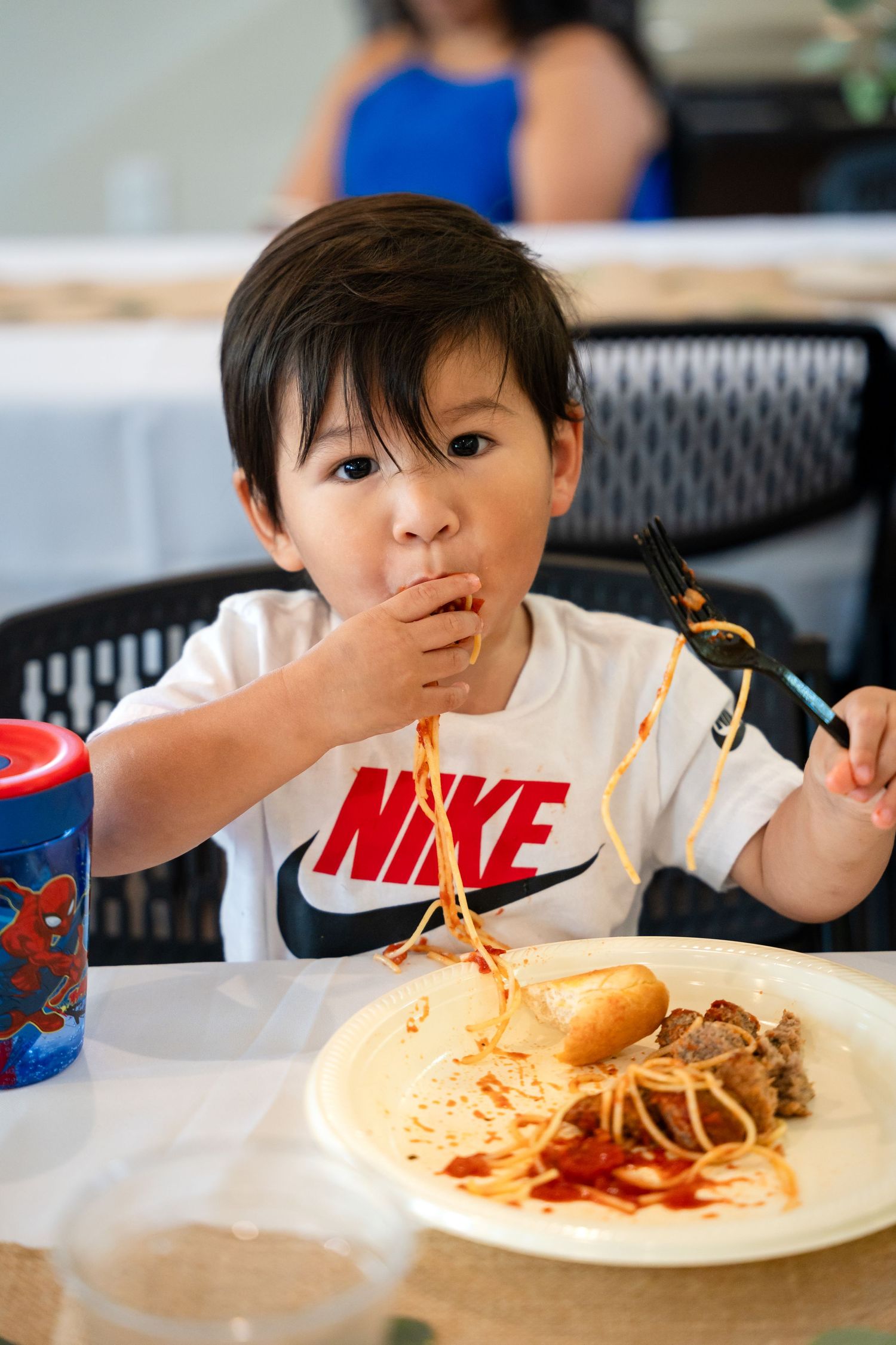 Young child in a Nike shirt enjoying spaghetti at a dining table with a drink.