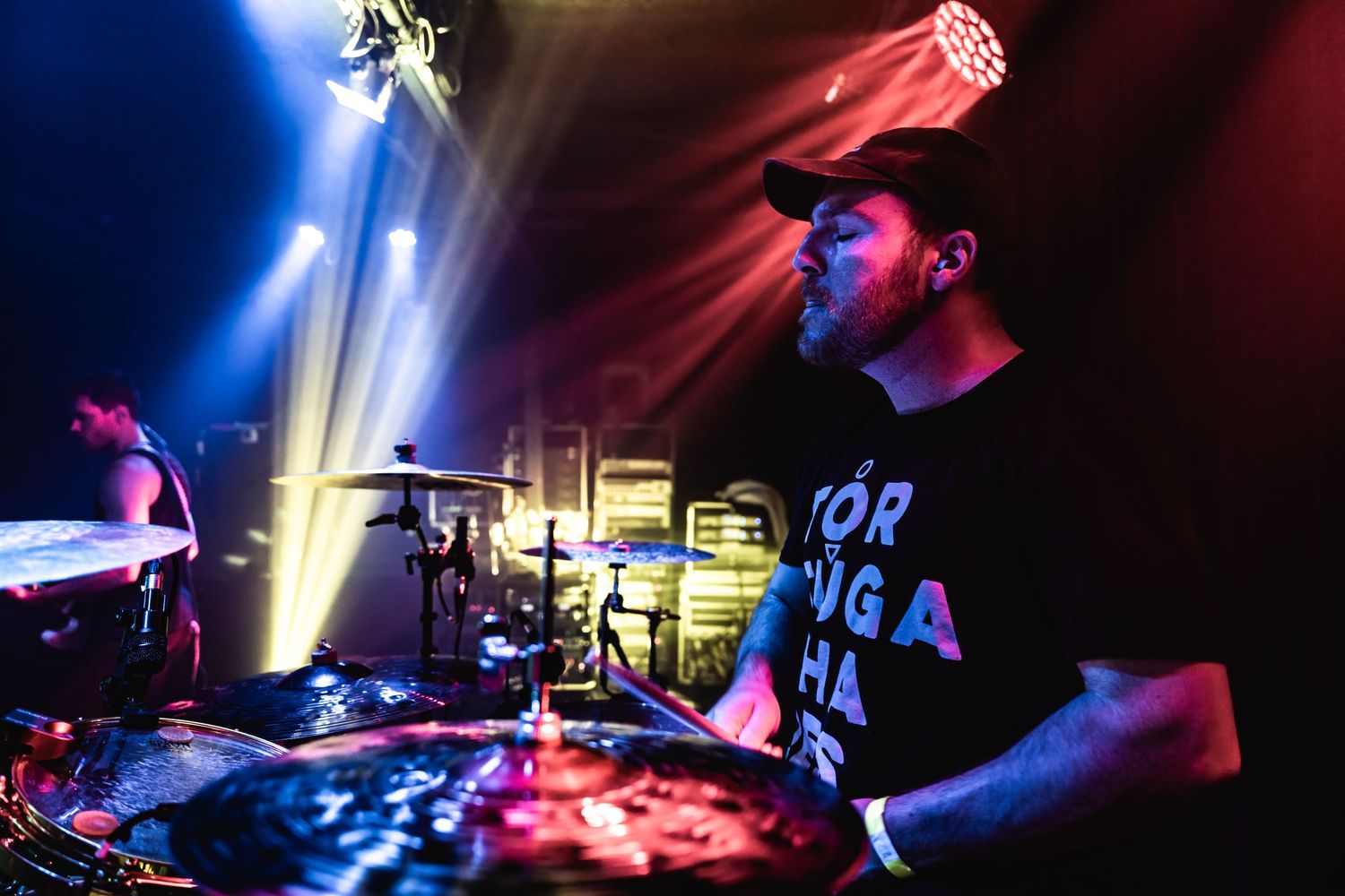 Drummer performing energetically with colorful stage lighting.