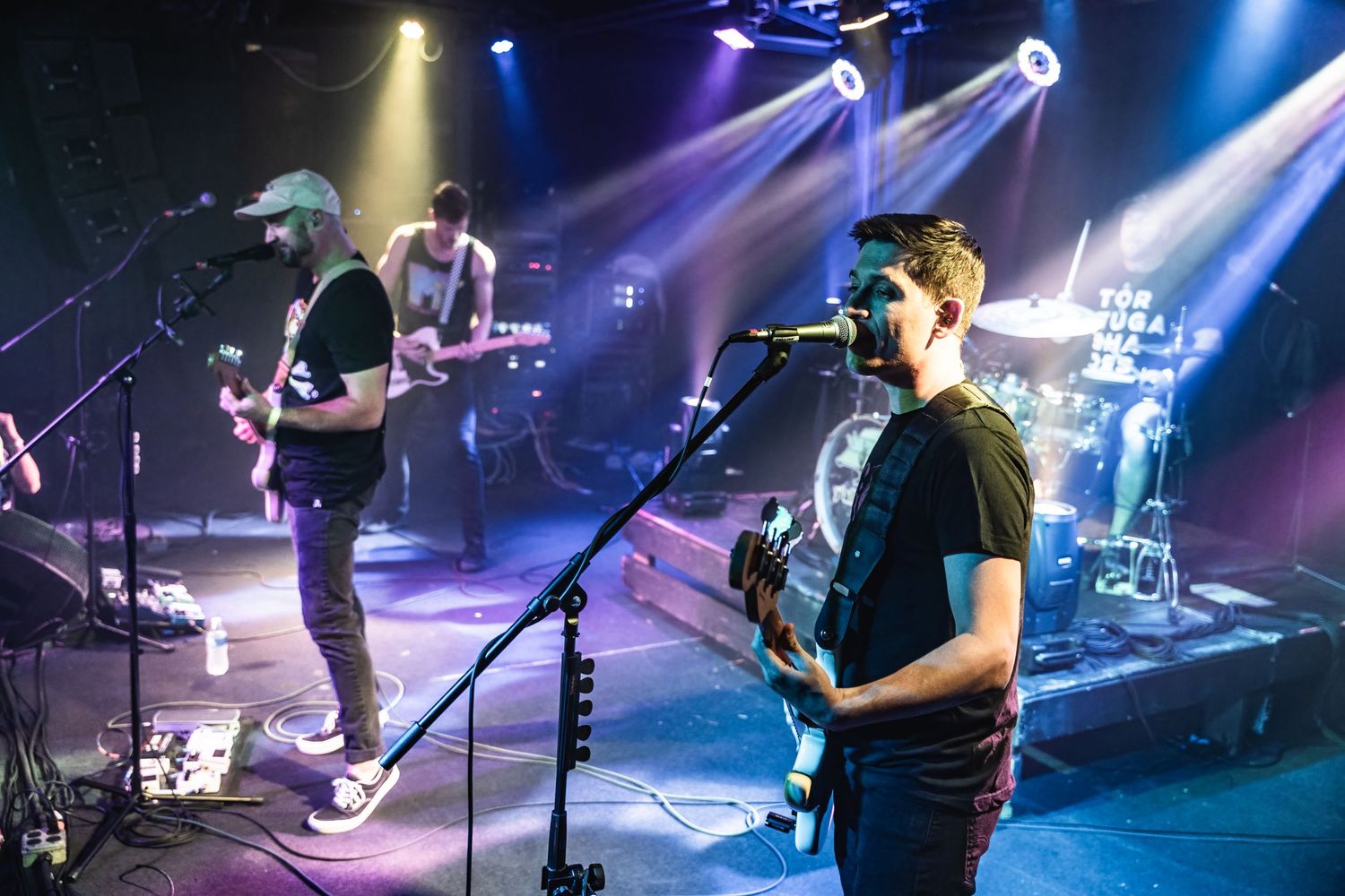 Band members perform on stage under dramatic blue and yellow spotlights during an energetic concert performance.