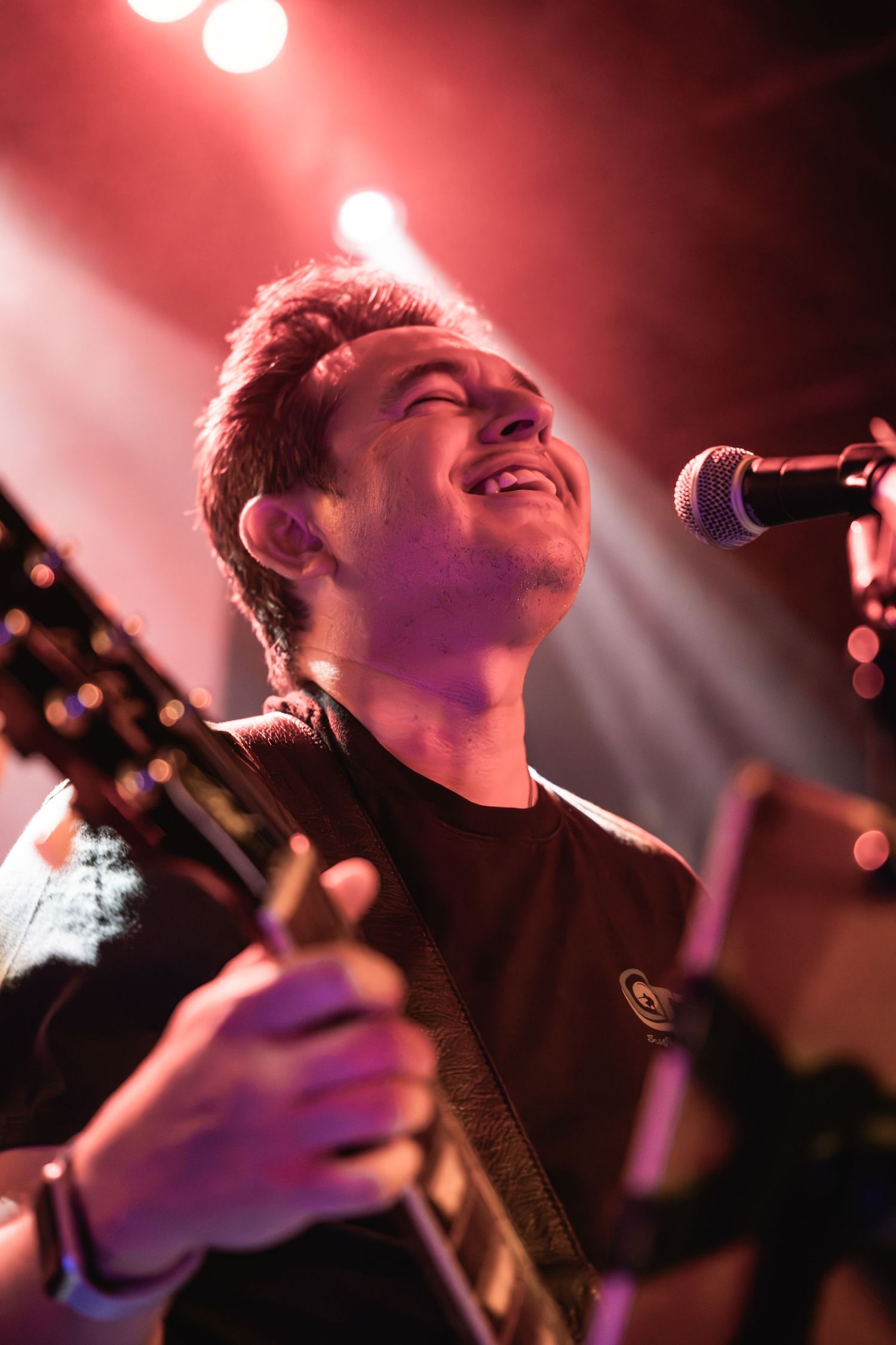 Performer singing and playing guitar with passionate expression under red spotlights.