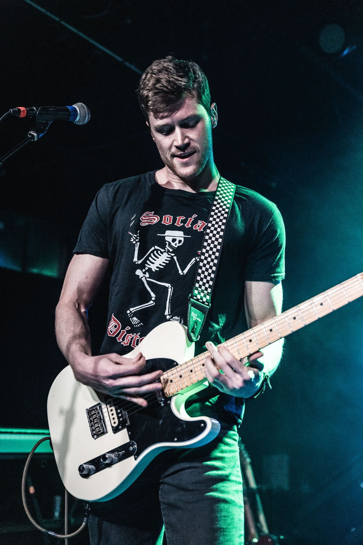 A musician playing a white electric guitar on stage with green lighting effects.