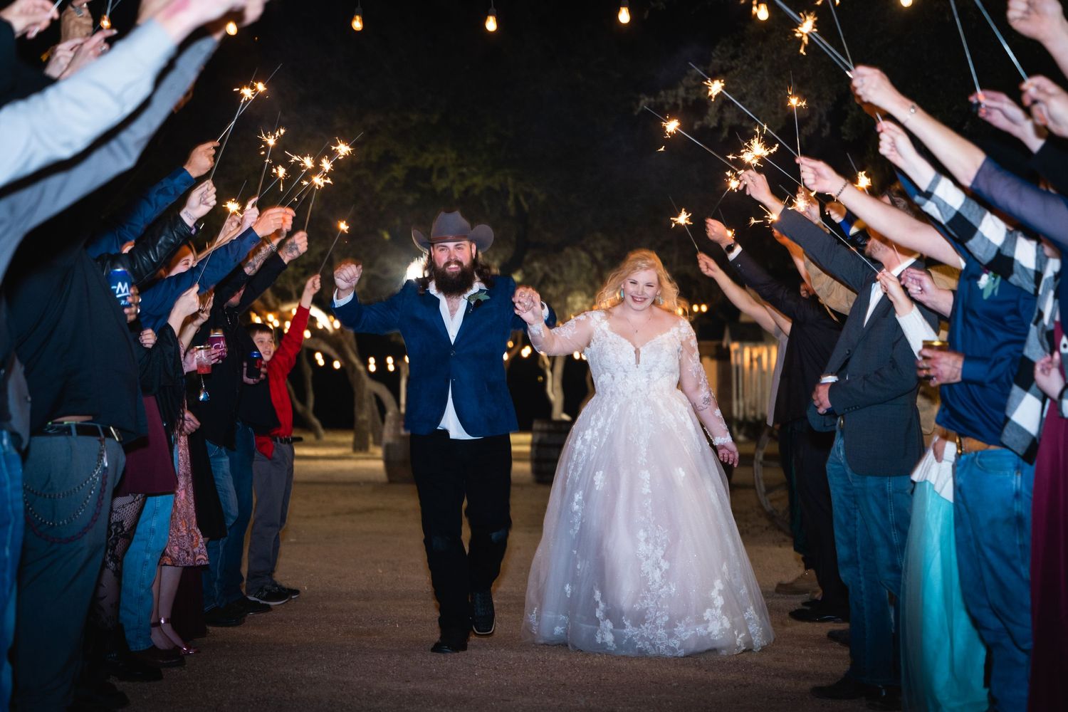 Guests hold sparklers forming a tunnel as newlyweds walk through during an evening wedding exit.
