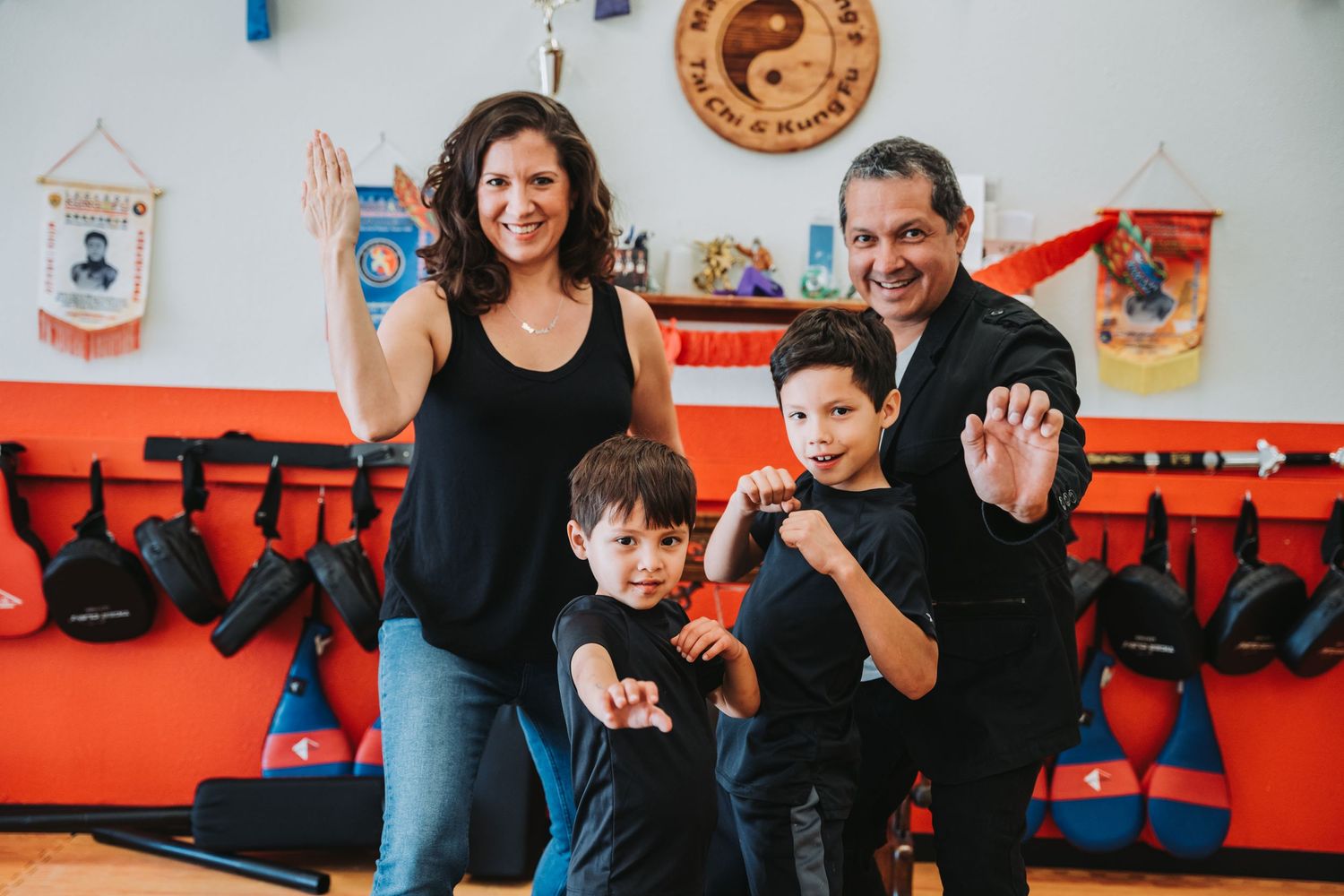 Family in martial arts poses together in studio with decorative belts on orange wall.