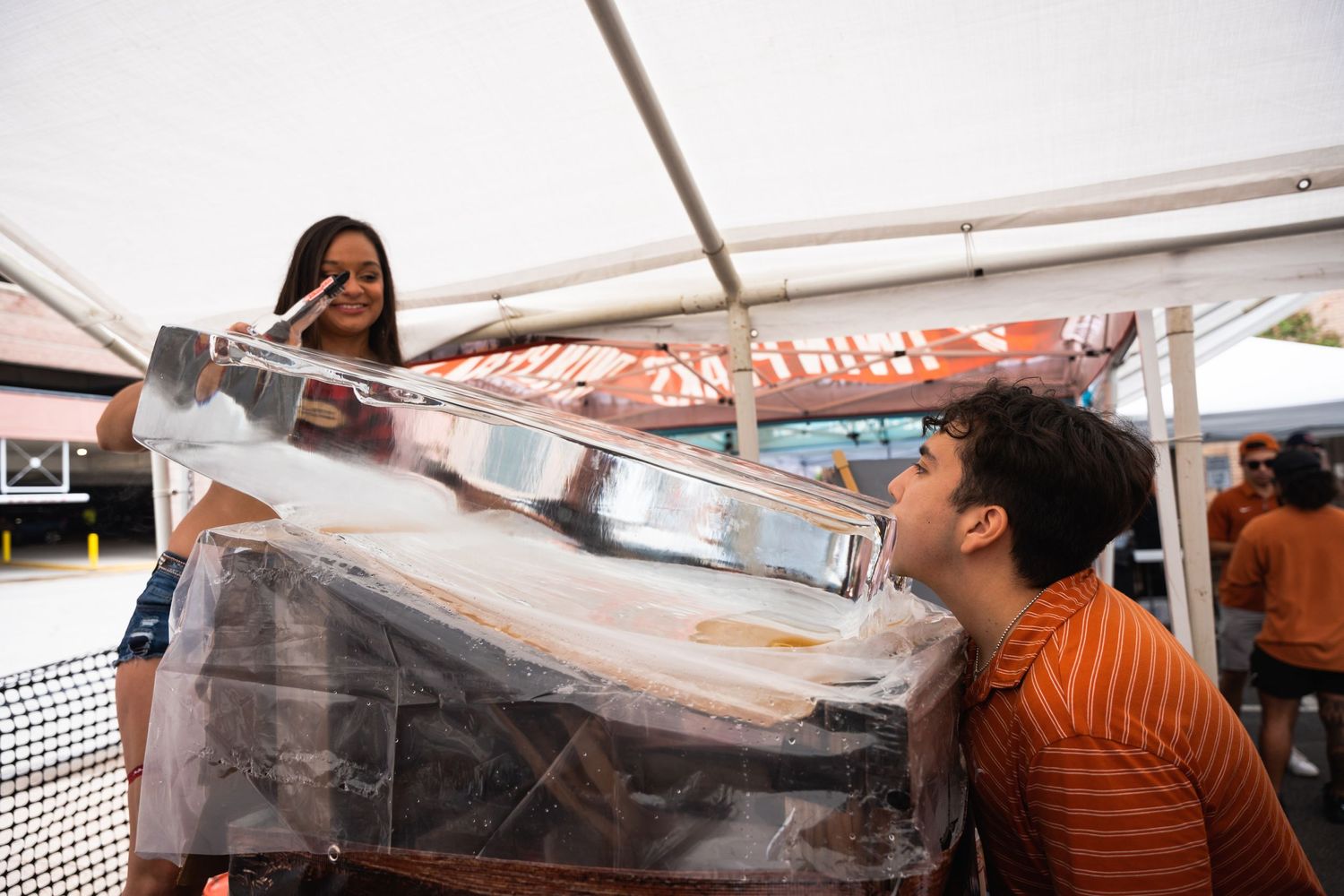 Two people having fun with a large beverage container at an outdoor event under a white tent.