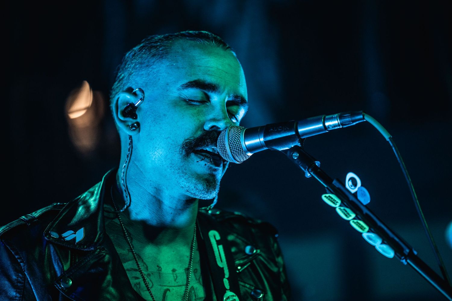 Close-up of performer singing into microphone with green theatrical lighting effects.