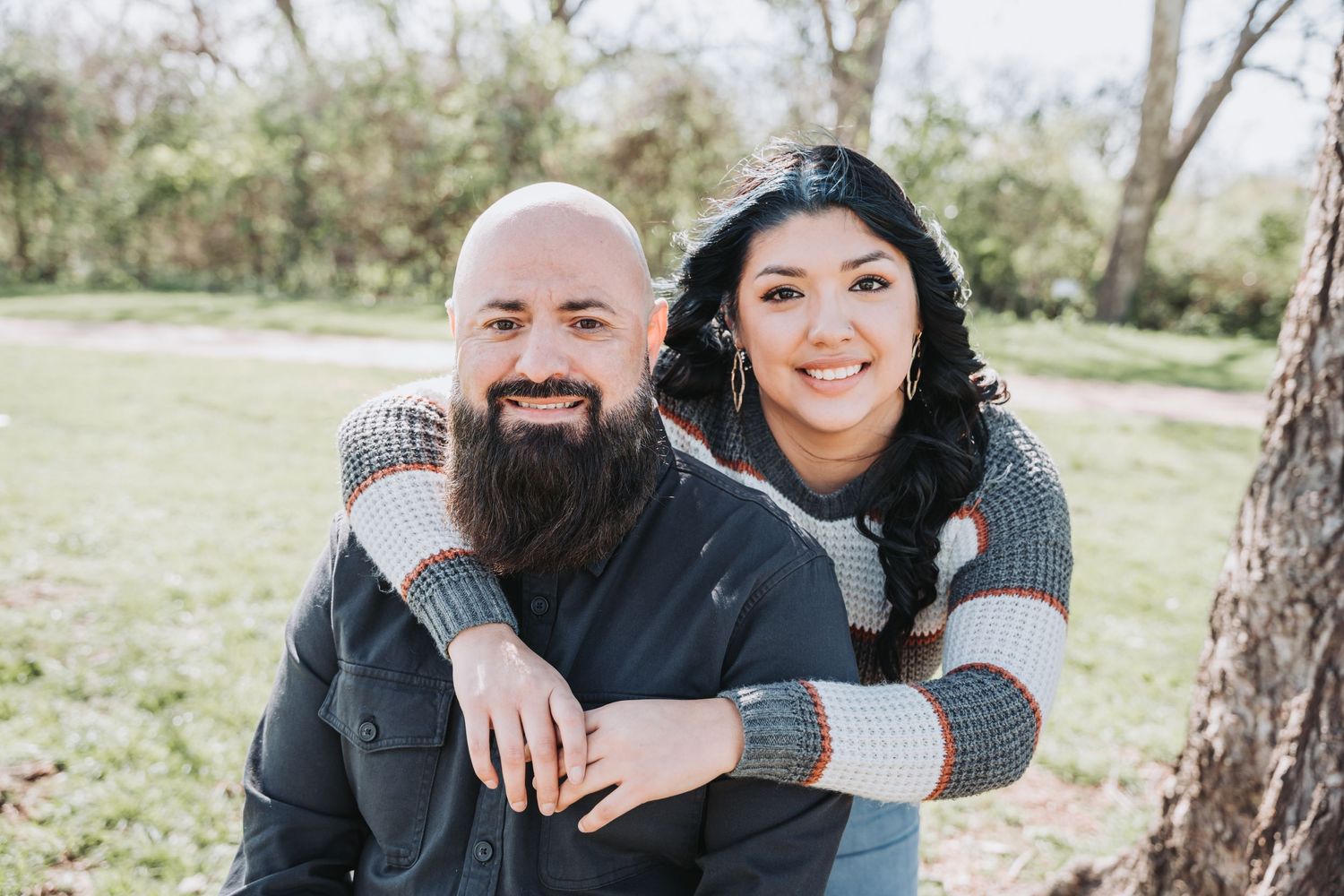 Couple embracing outdoors with one wearing grey sweater and other in black shirt.