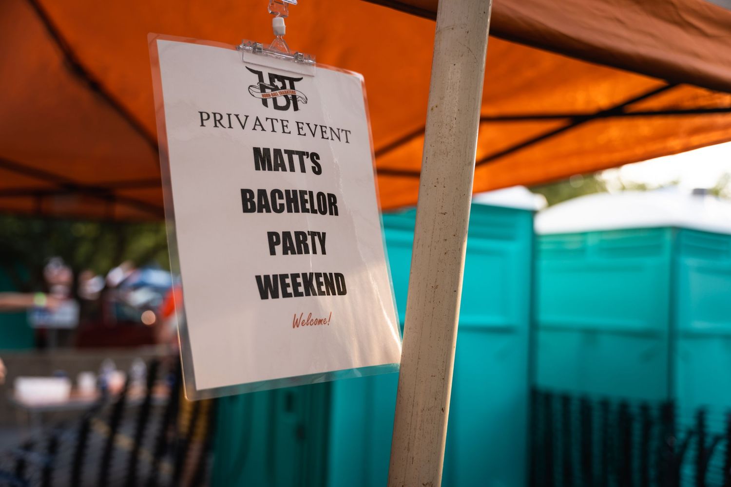 Close-up of hanging sign for Matt's Bachelor Party Weekend under orange tent.