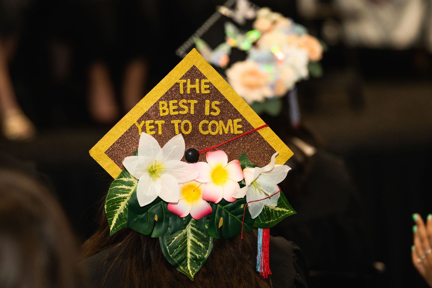 A decorated graduation cap reads 'The Best Is Yet To Come' with floral decorations.