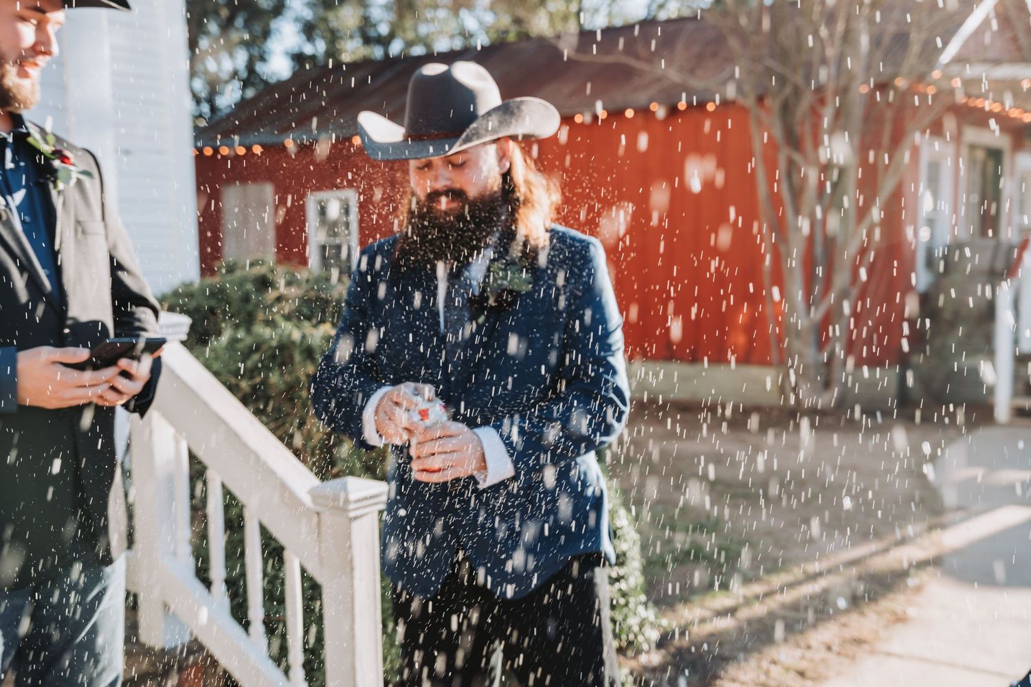 Snow falls while people celebrate on a porch with wooden railings.