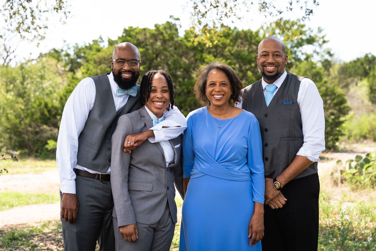 Small group in formal attire with matching vests and dresses poses outdoors.