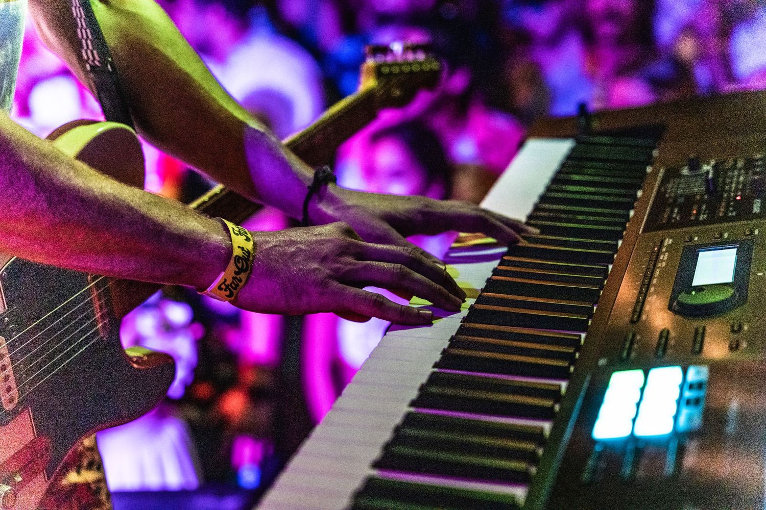 Musicians hands playing a keyboard with purple stage lighting in the background.