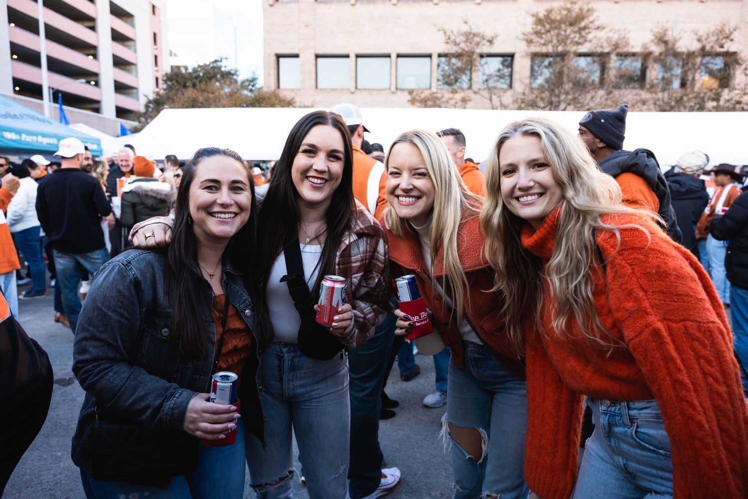 Friends holding beverages pose together at an outdoor sports tailgate party.