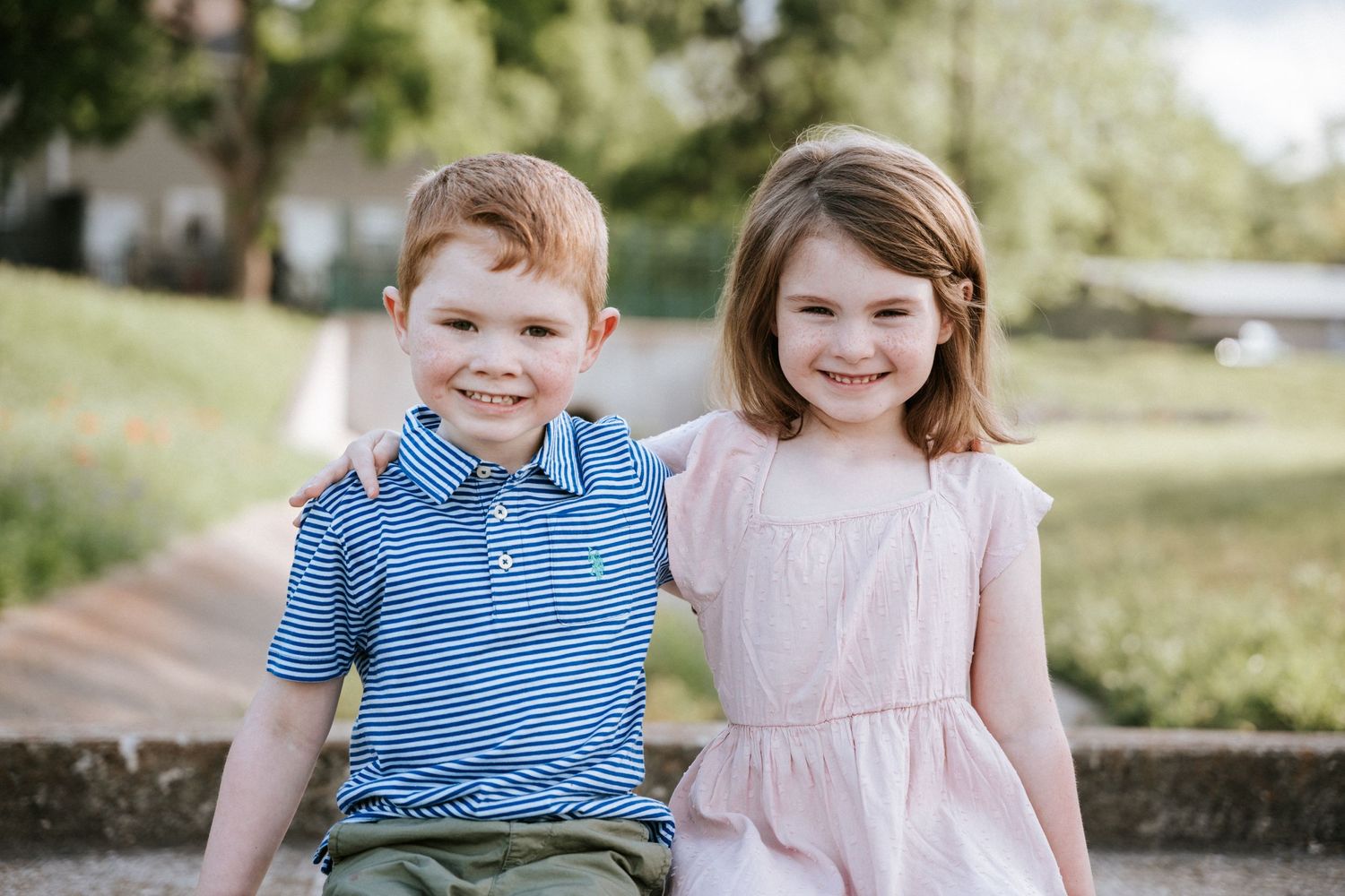 Two children sit together on concrete steps on a sunny day.