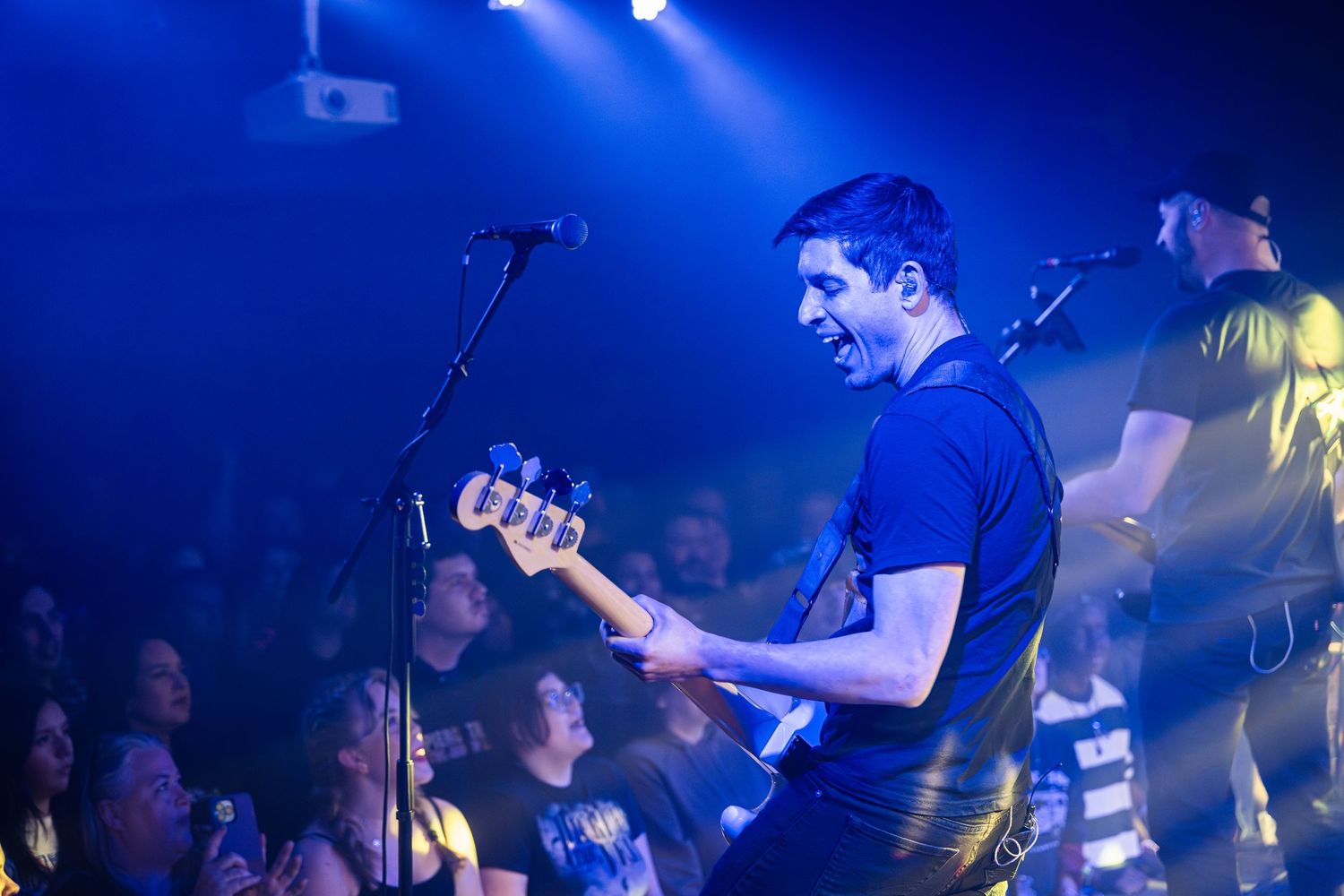 A musician performs on stage bathed in blue lighting while an enthusiastic crowd watches.