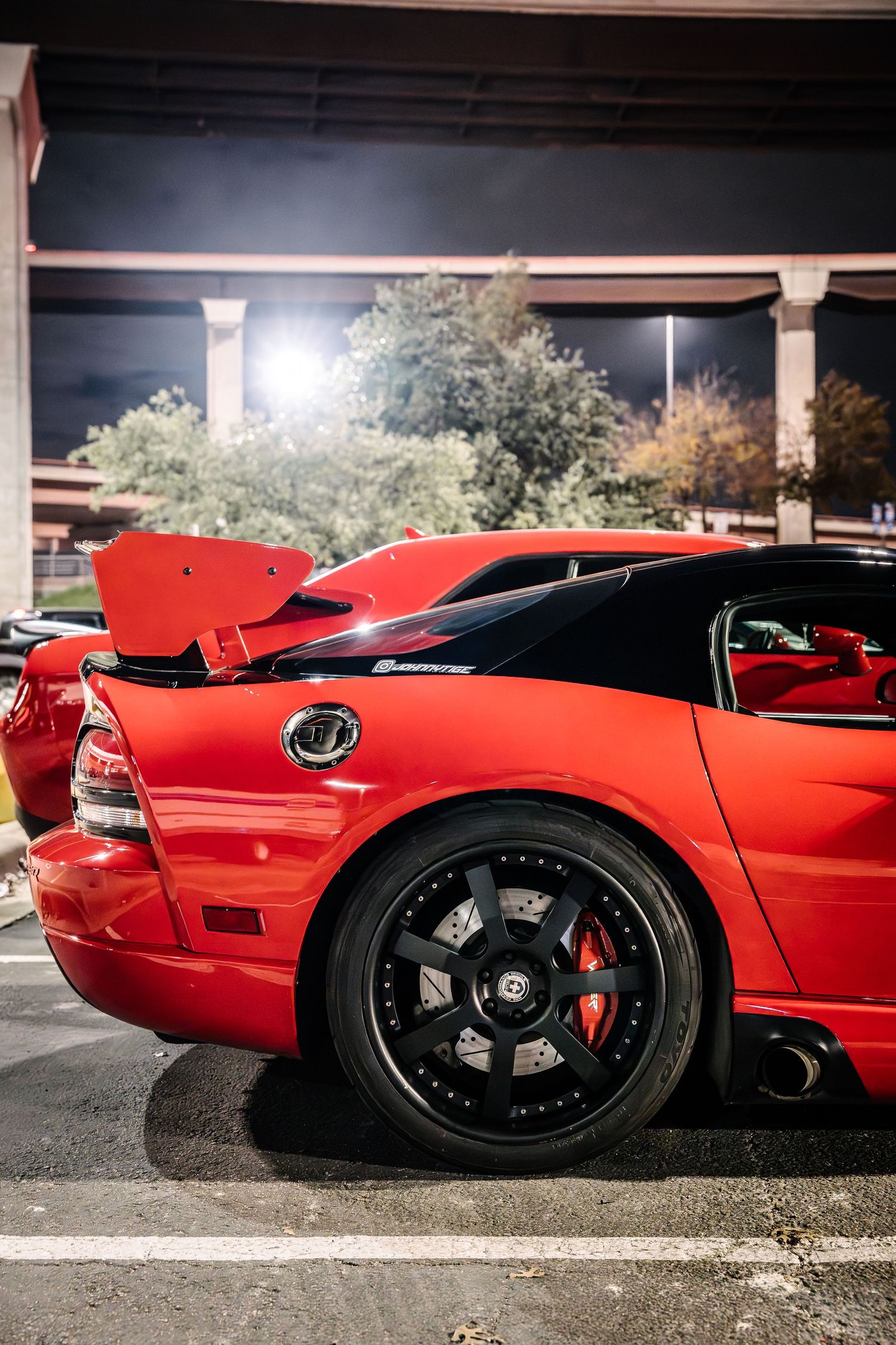 A red sports car with black wheels parked under a structure at night.